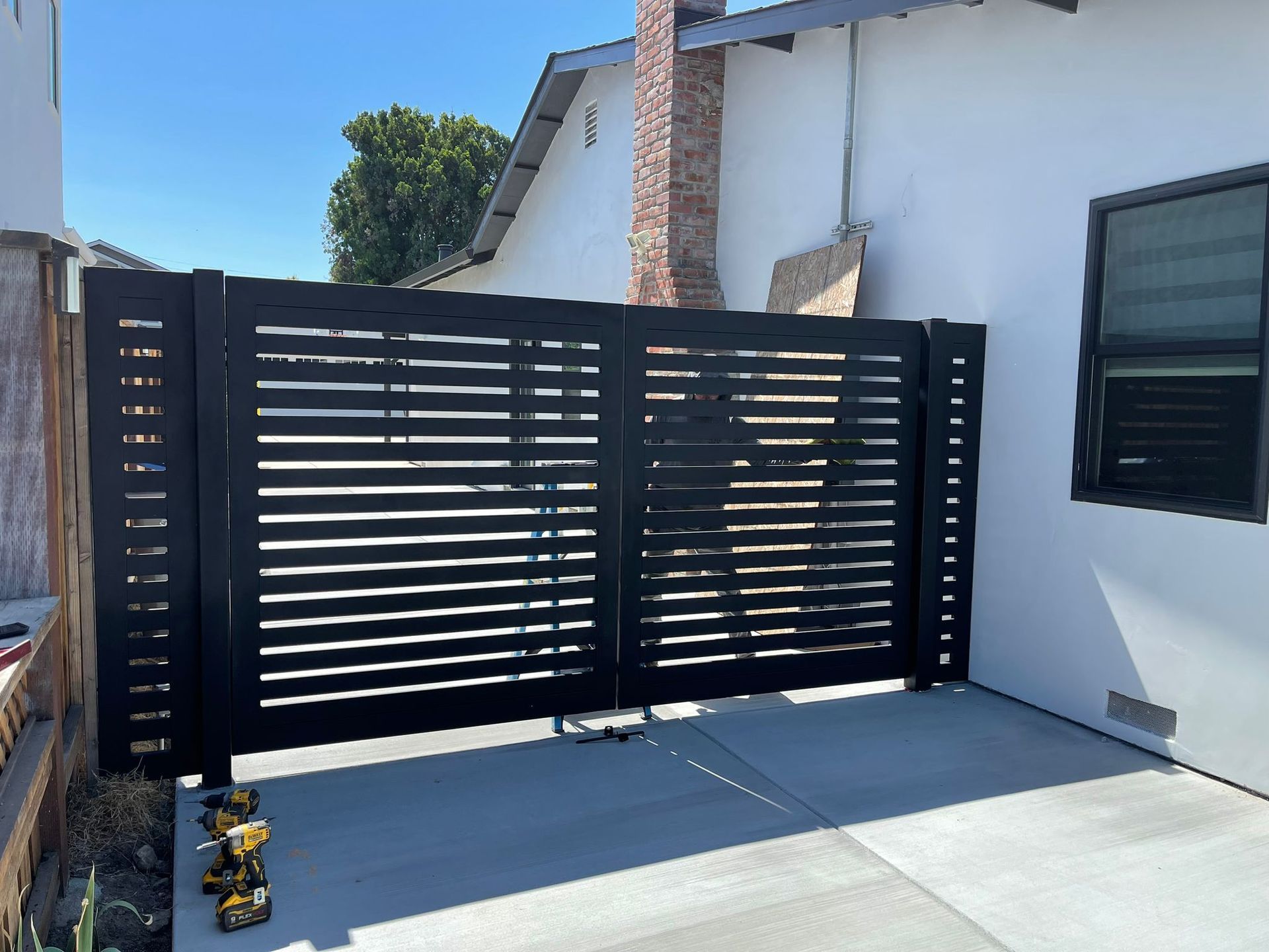 Black horizontal slat gate against a white house and blue sky.