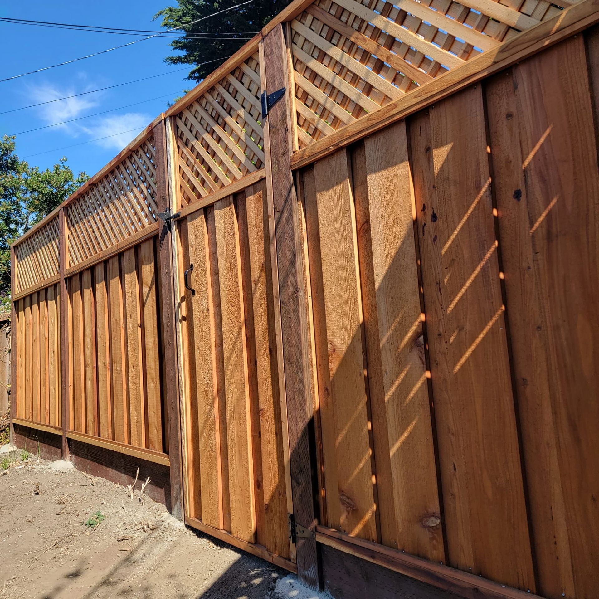 Wooden fence with lattice top, casting shadows in sunlight.