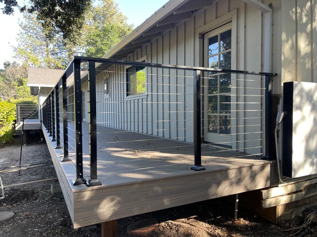 Deck with black railing and wire, attached to a white-sided building with a door.