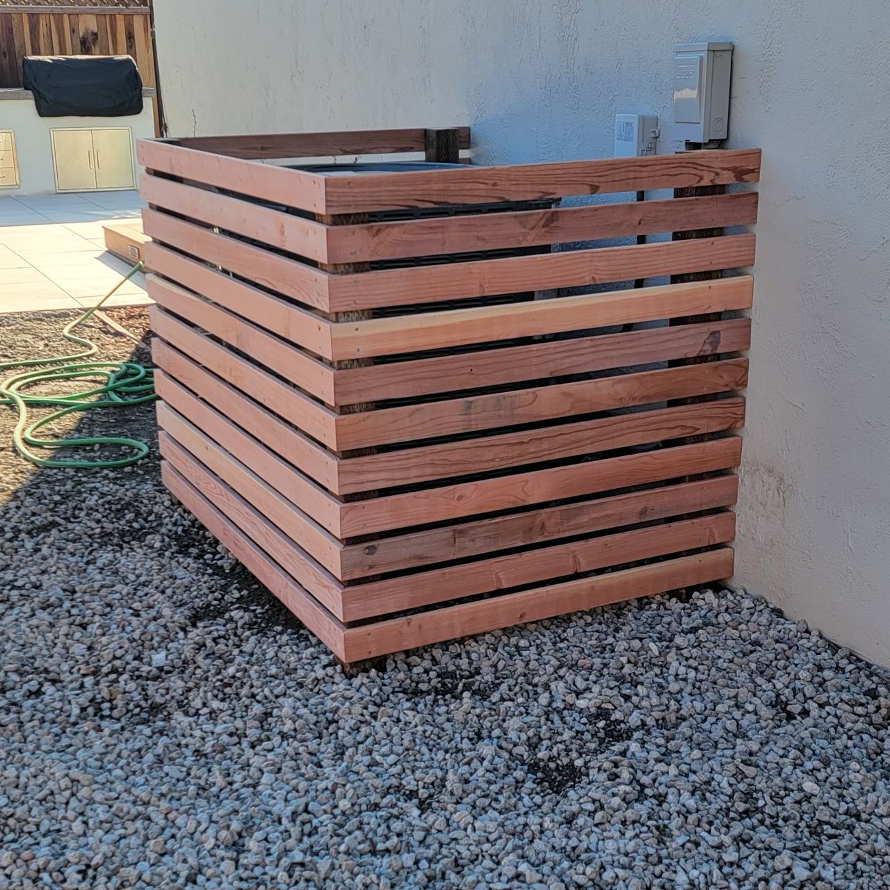 Wooden air conditioner enclosure on gravel, attached to a white wall.