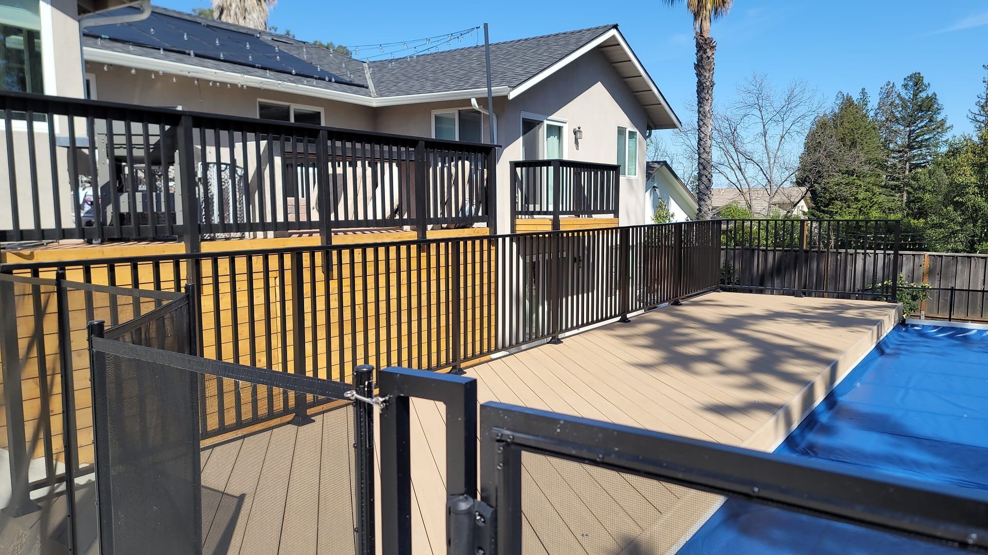 Two-story house with a wooden deck and stairs under construction. A worker uses a table saw.