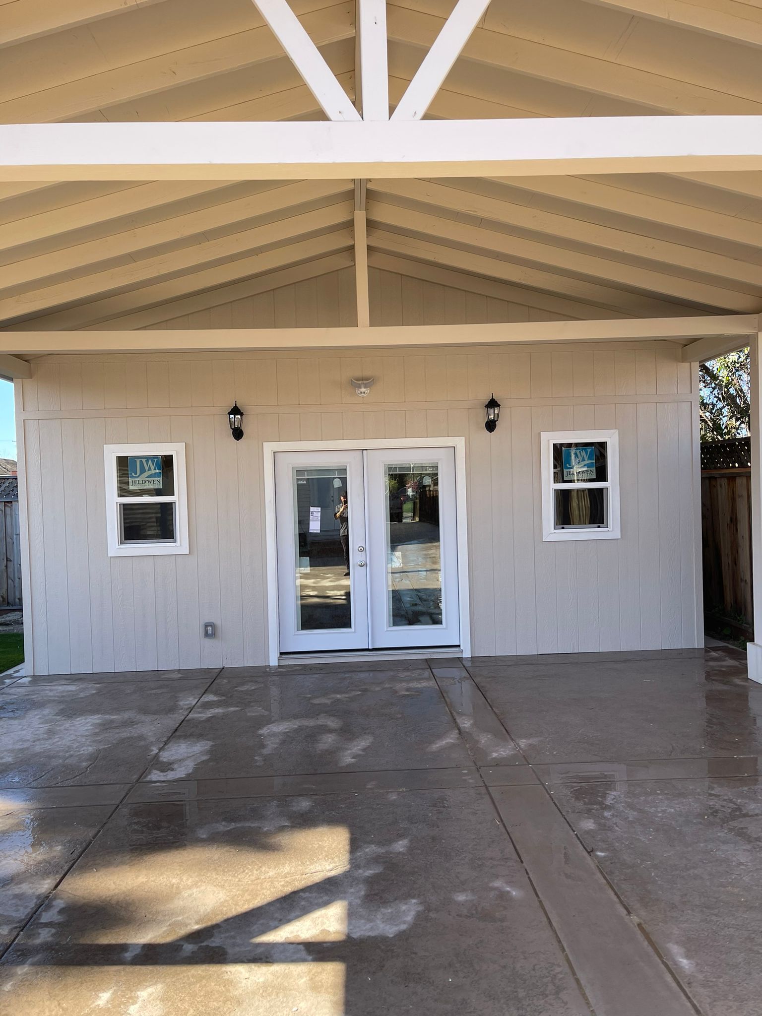 Tan covered patio with double glass doors, windows, and two black sconces.