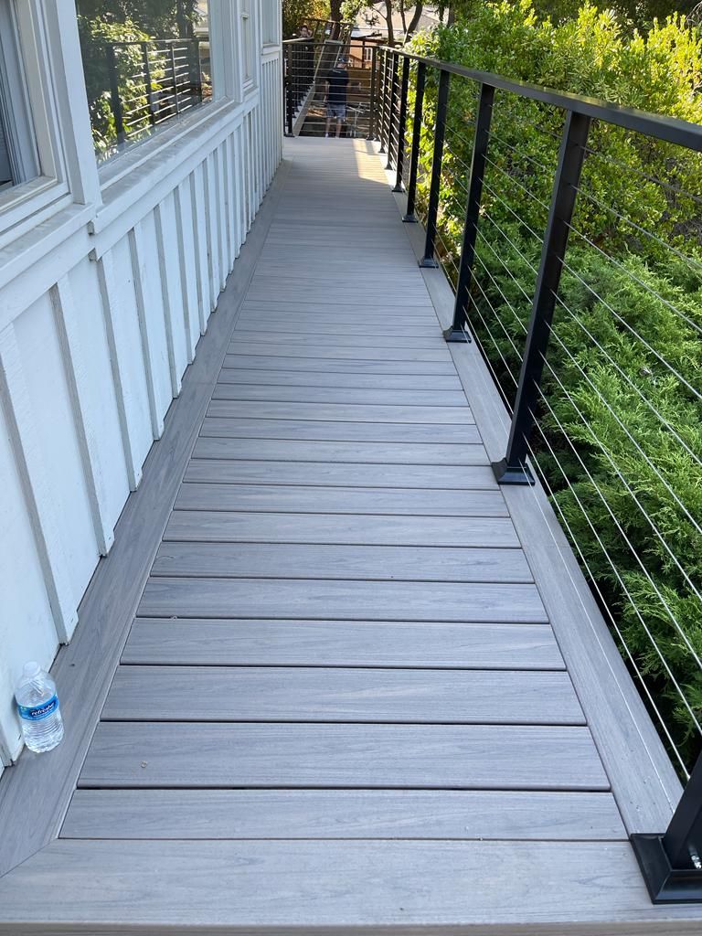 Wooden deck with cable railing beside a house with white siding and a view of trees.