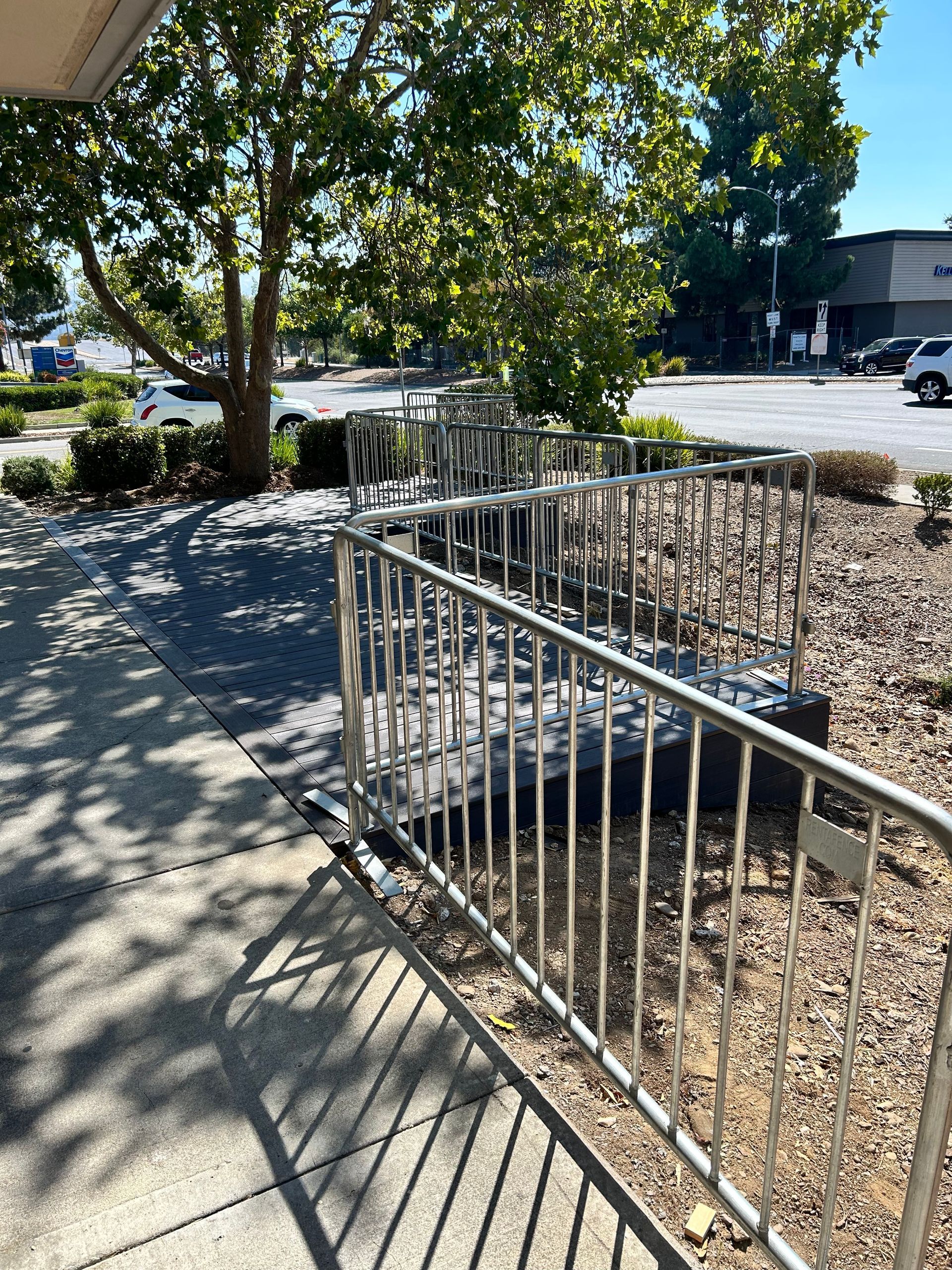 Outdoor ramp with metal railings leading to a building entrance. Gray gravel and a tree are nearby.