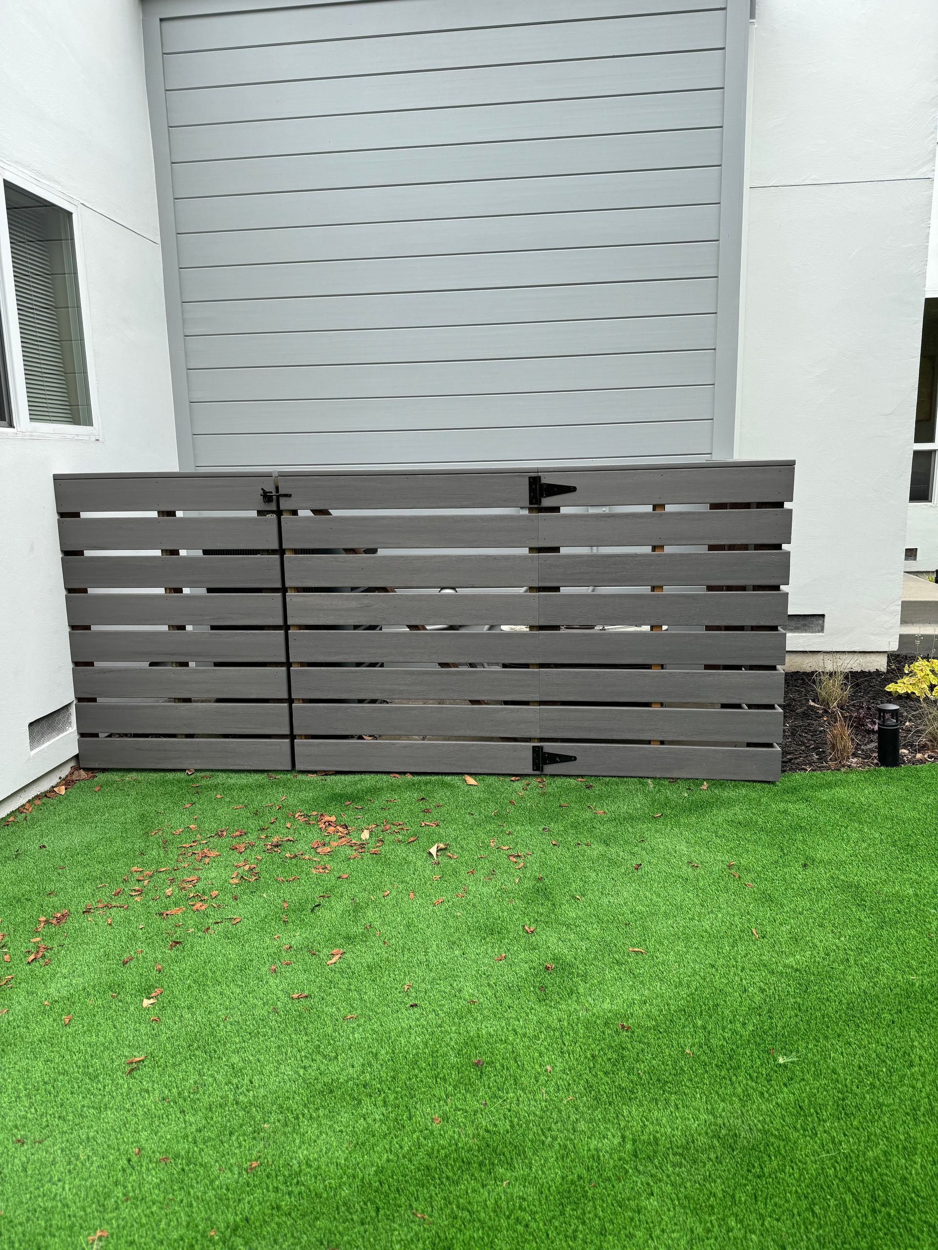 Gray horizontal slat enclosure with a hinged door on artificial turf.