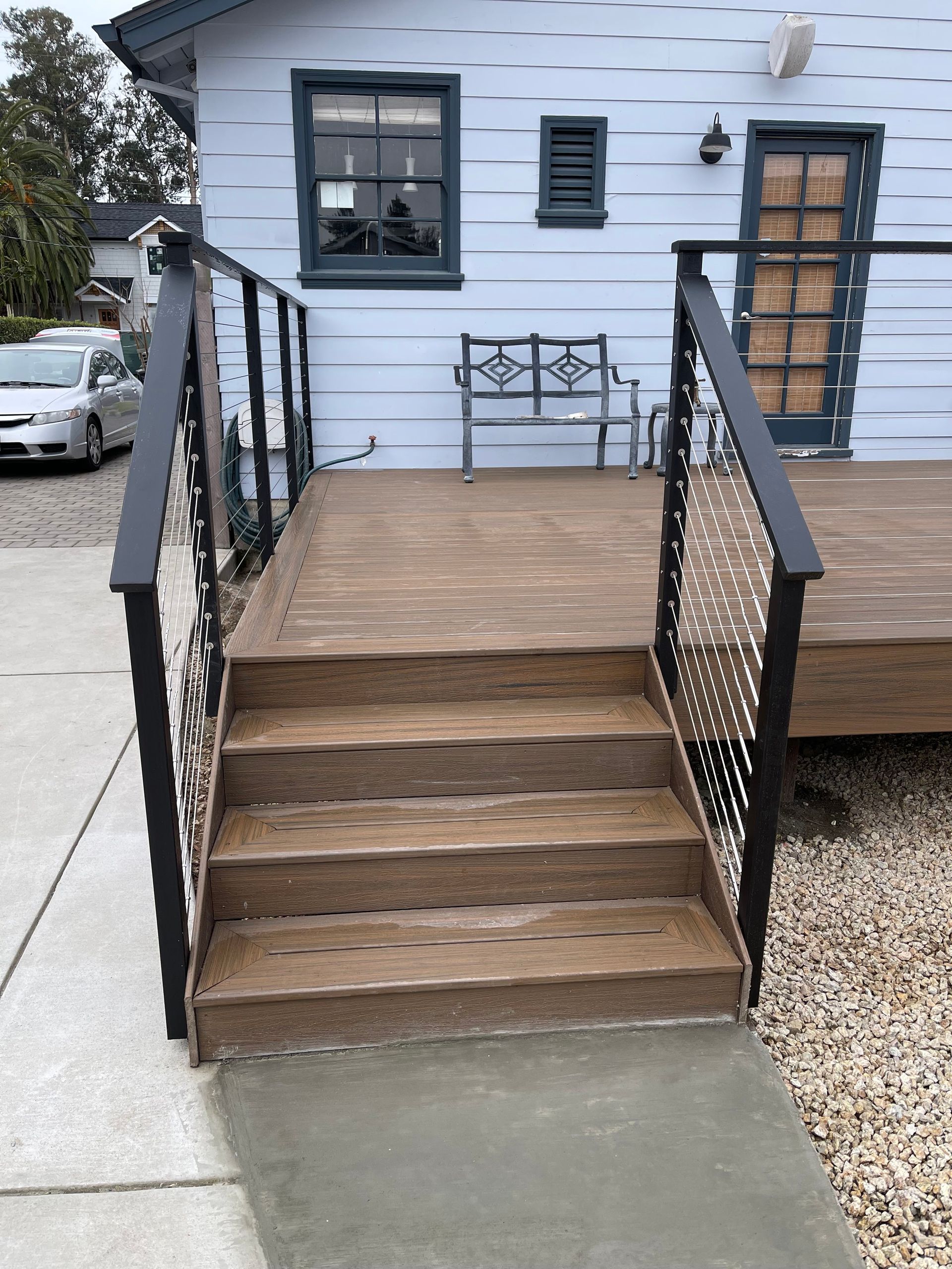 Wooden steps leading up to a deck with metal railing; a blue building is in the background.