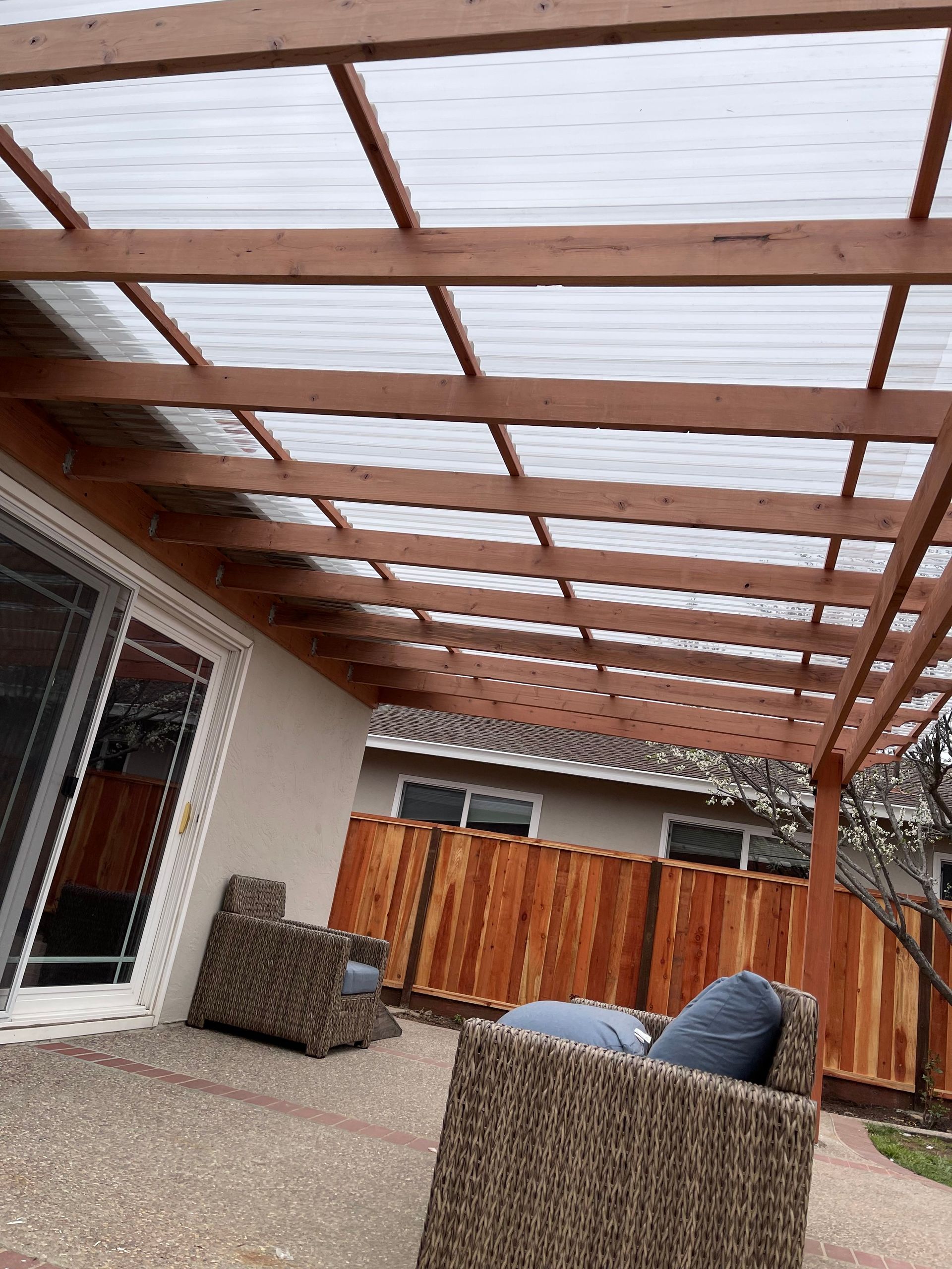 Patio with wooden pergola and clear roof over seating area.