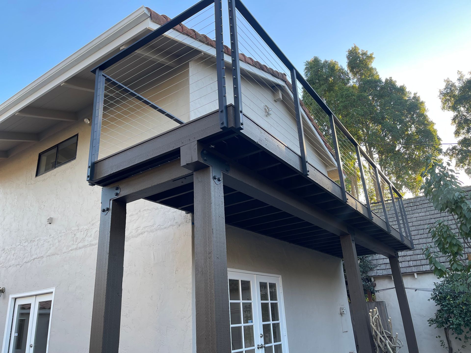 Elevated outdoor deck with black metal railing and supports attached to a stucco building.