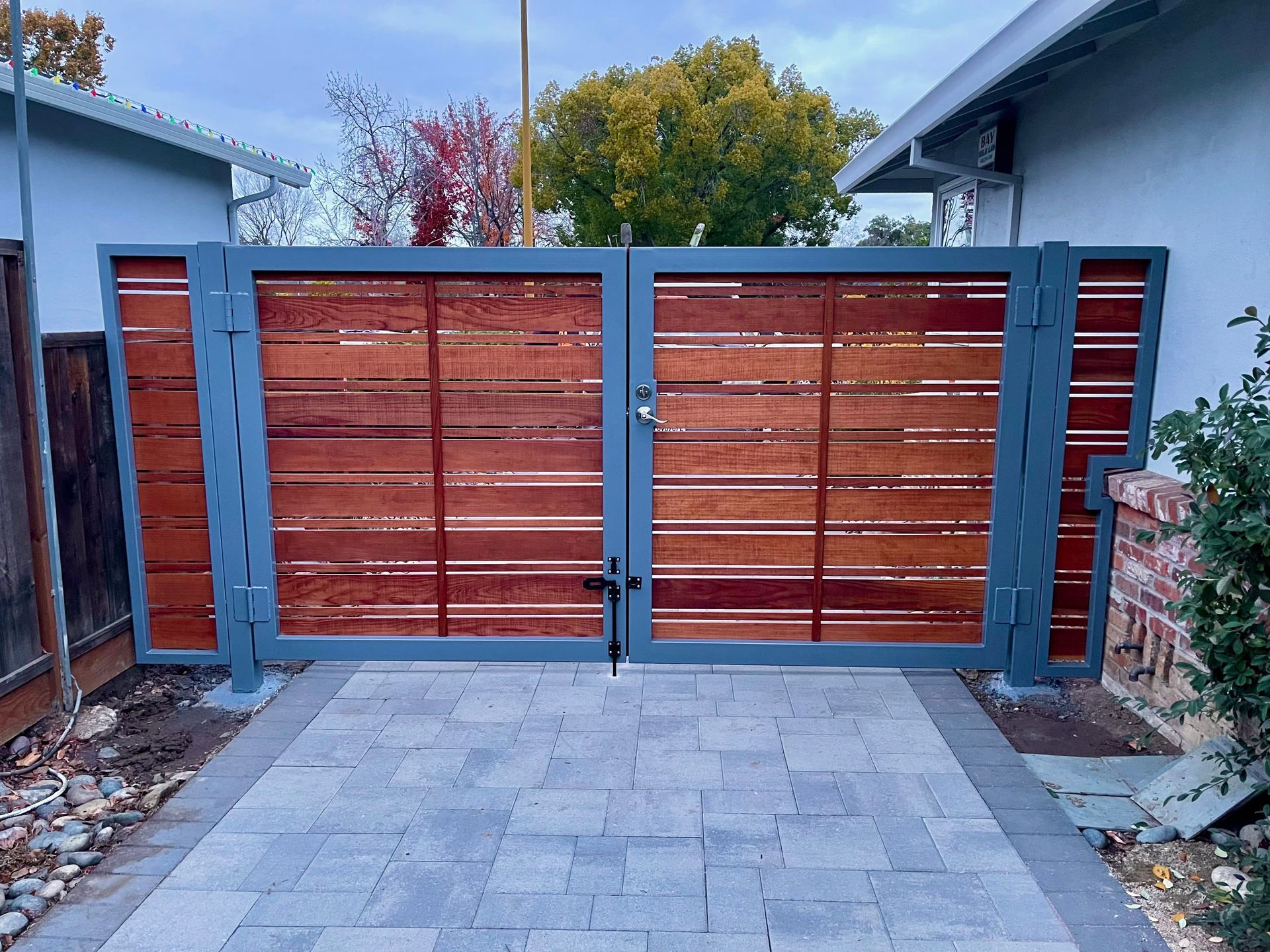 Double wooden gate with horizontal planks, metal frame, set in brick pathway.