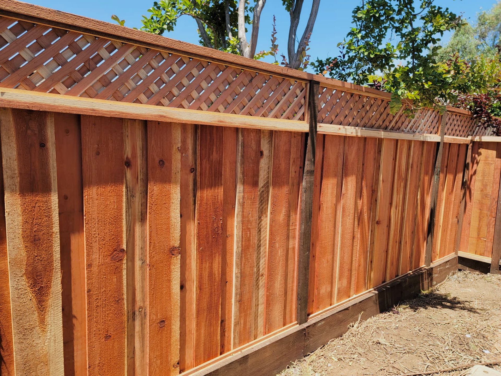 Wooden fence with lattice top, stained reddish-brown, in a sunny outdoor setting.