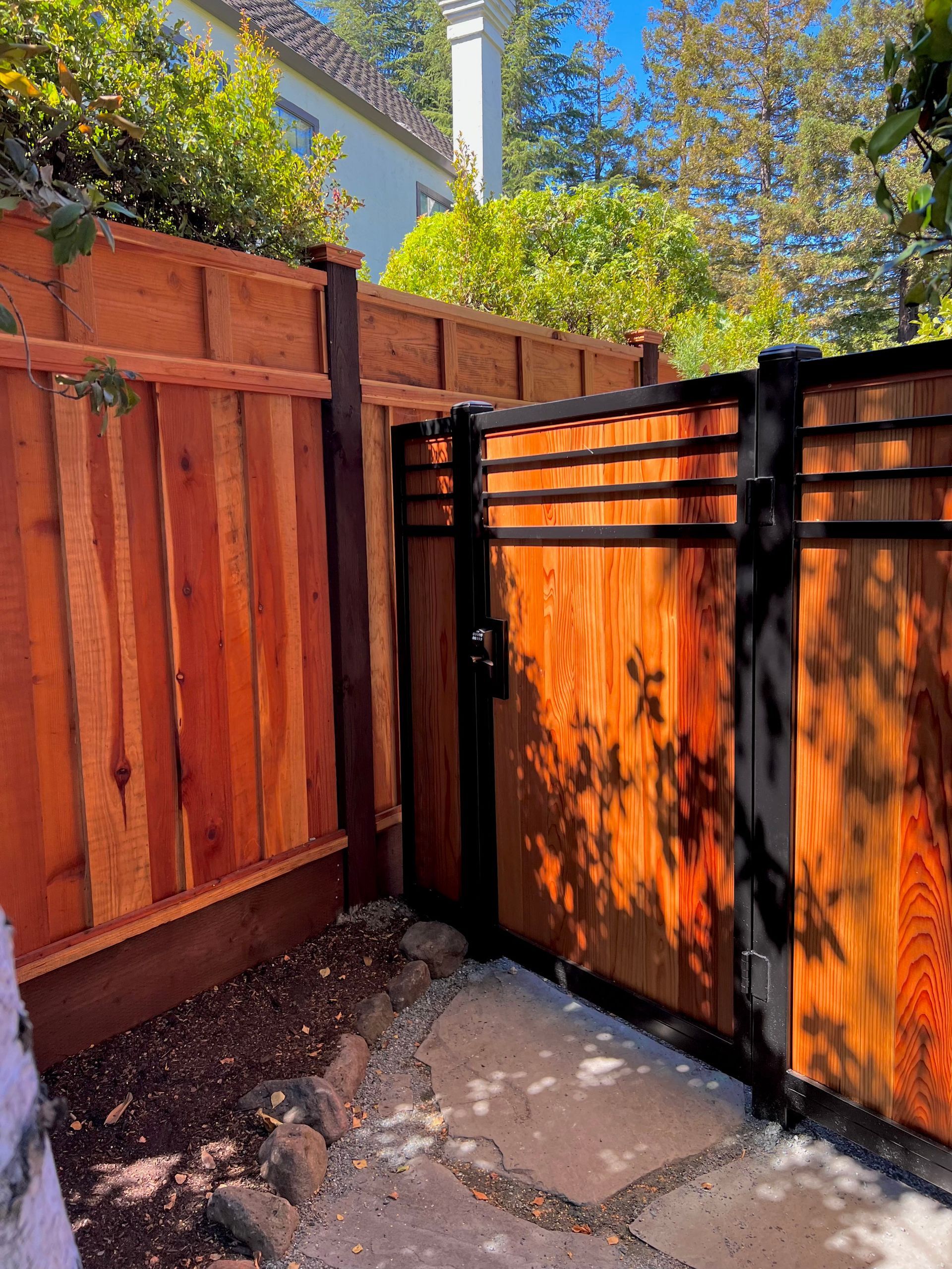 Wooden fence with gate, featuring black metal accents. Sunny outdoor setting.