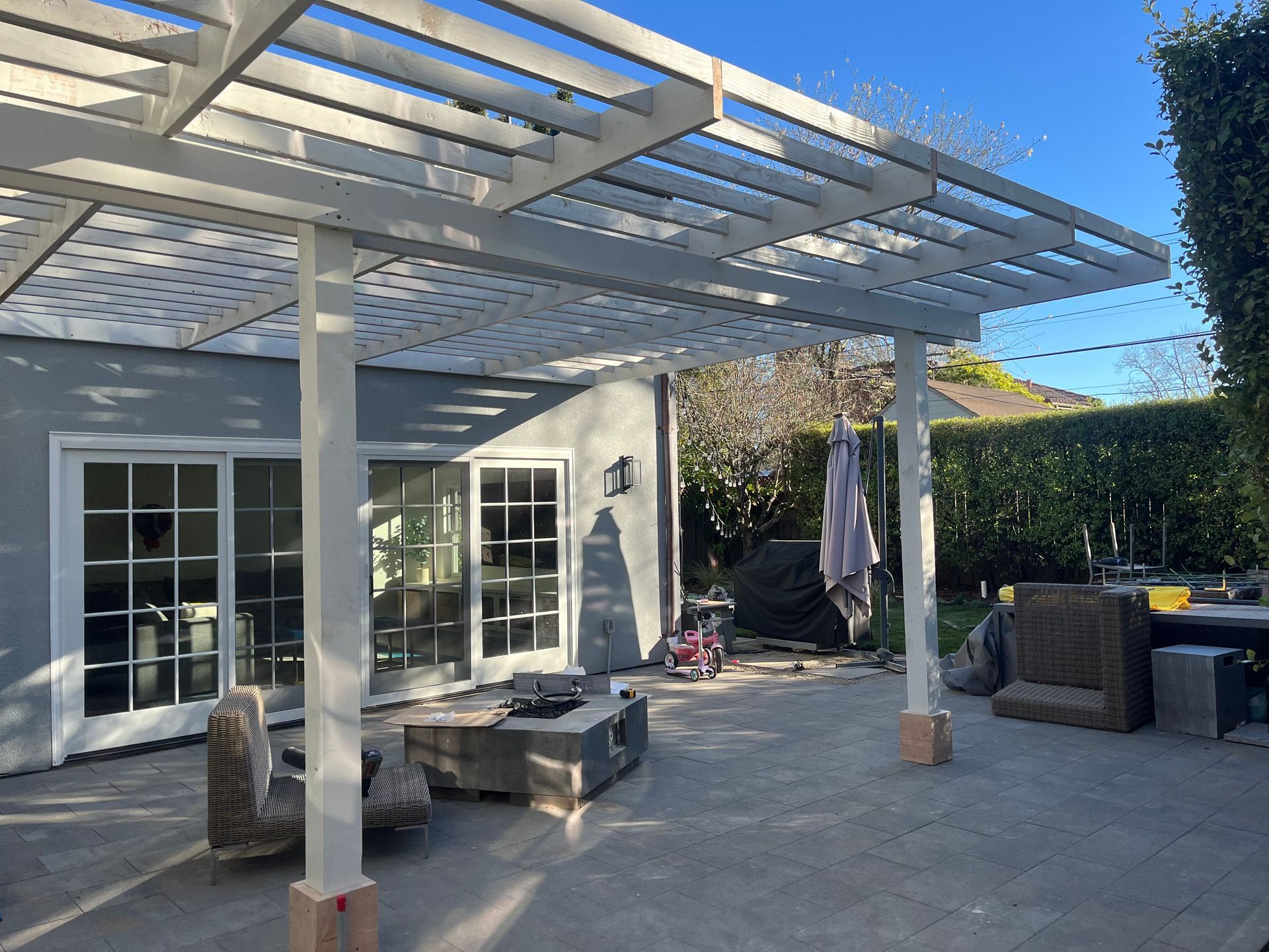 Backyard patio with a white pergola, fire pit, and sliding glass doors.