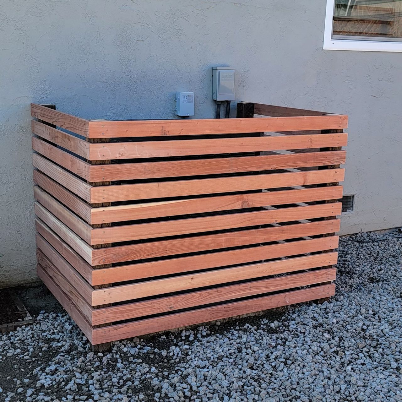 Wooden slat enclosure around an air conditioning unit against a gray wall.