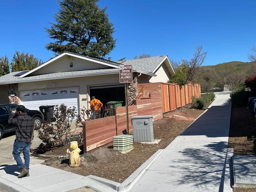 Man taking photo in front of house with open garage, new wood fence, sidewalk, and fire hydrant.