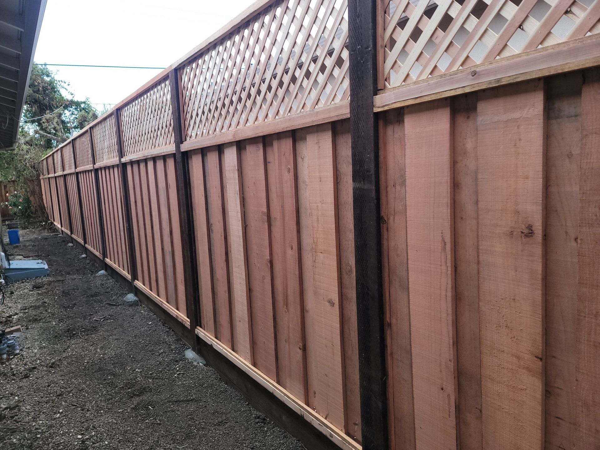 Wooden fence with lattice top, stained reddish-brown, along a gravel path.