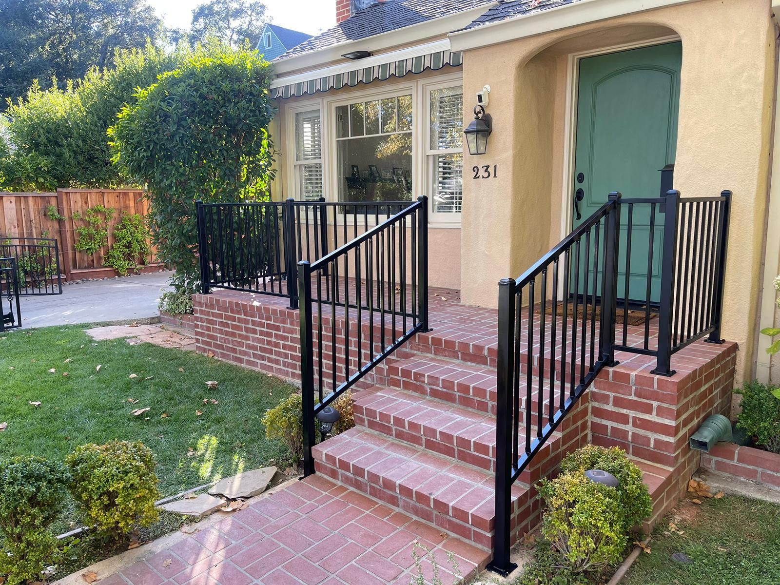 A house with brick steps, a green door, and black railings. Number 