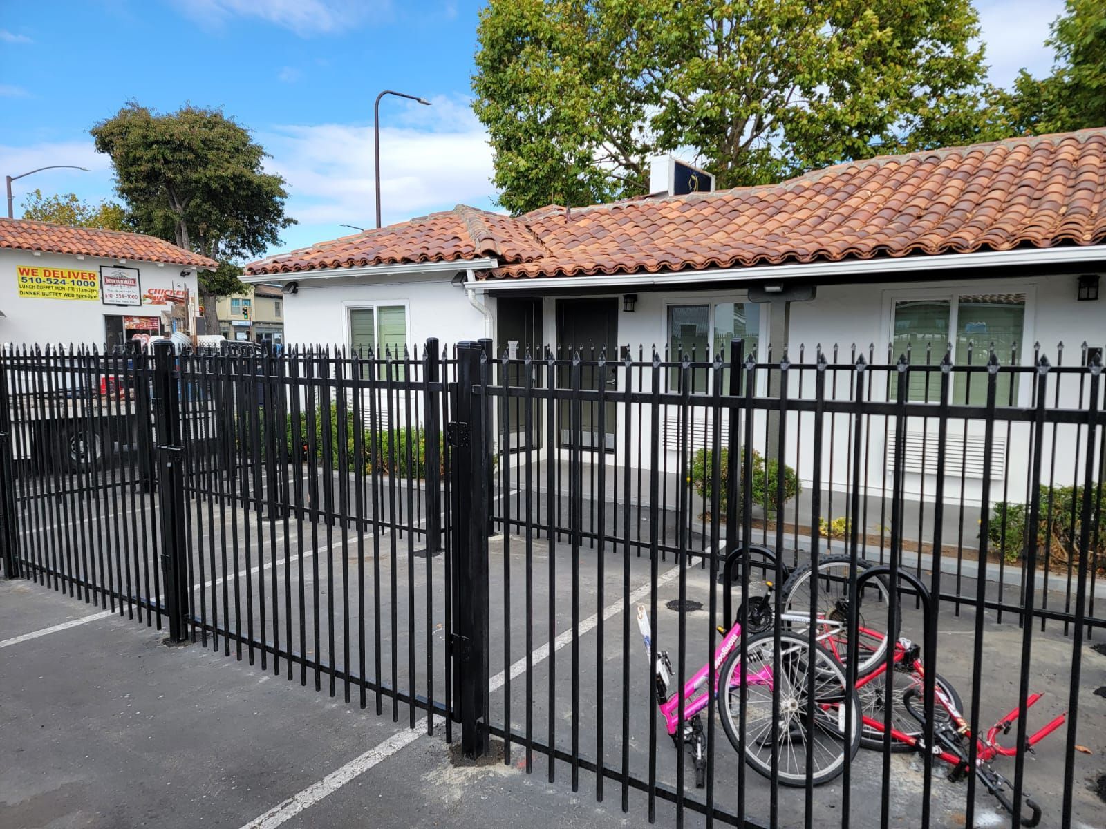 Black metal fence in front of a white building with an orange tiled roof. Two parked bikes.