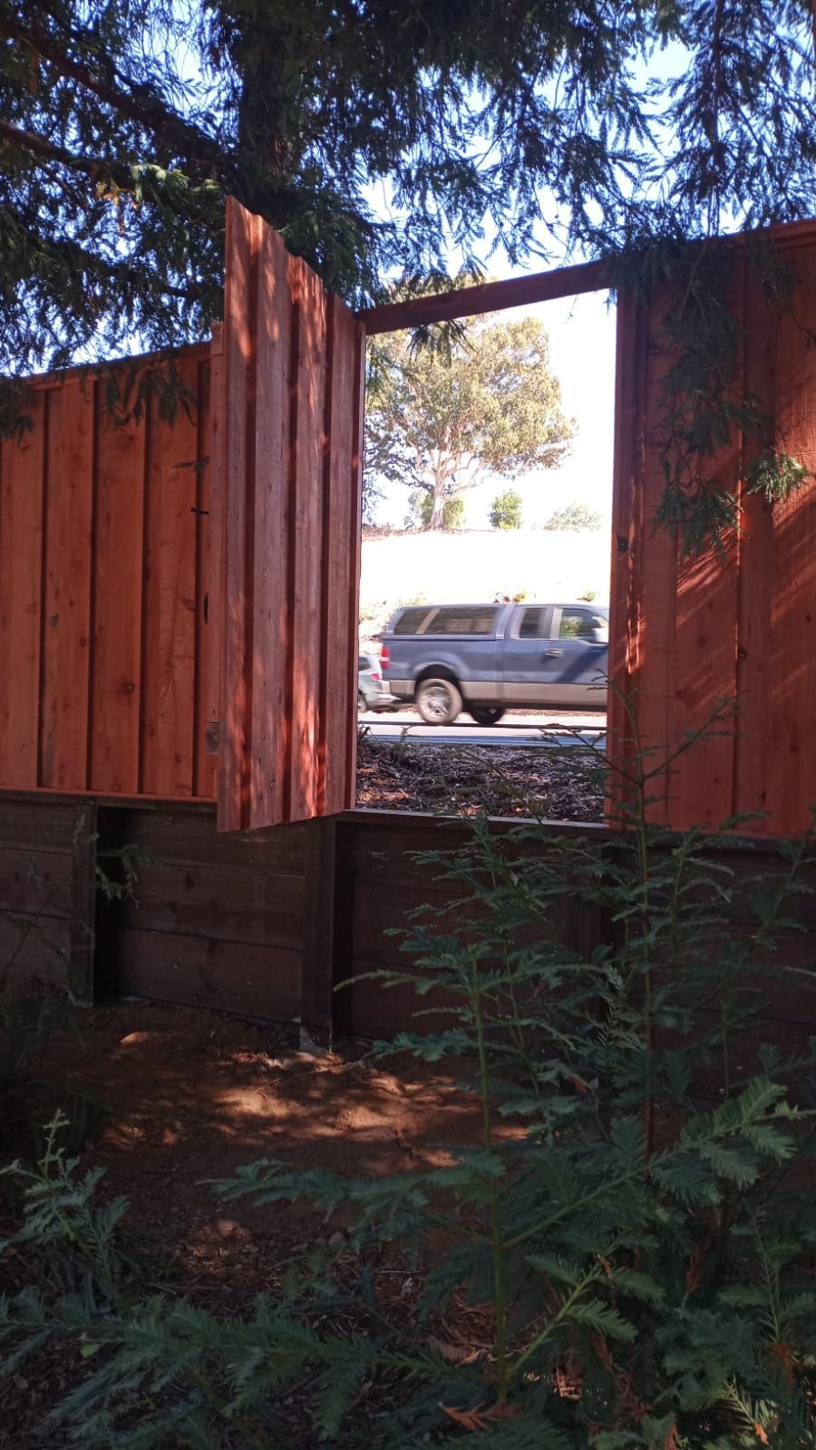 Wooden fence gate open, framing a view of a truck on the road.