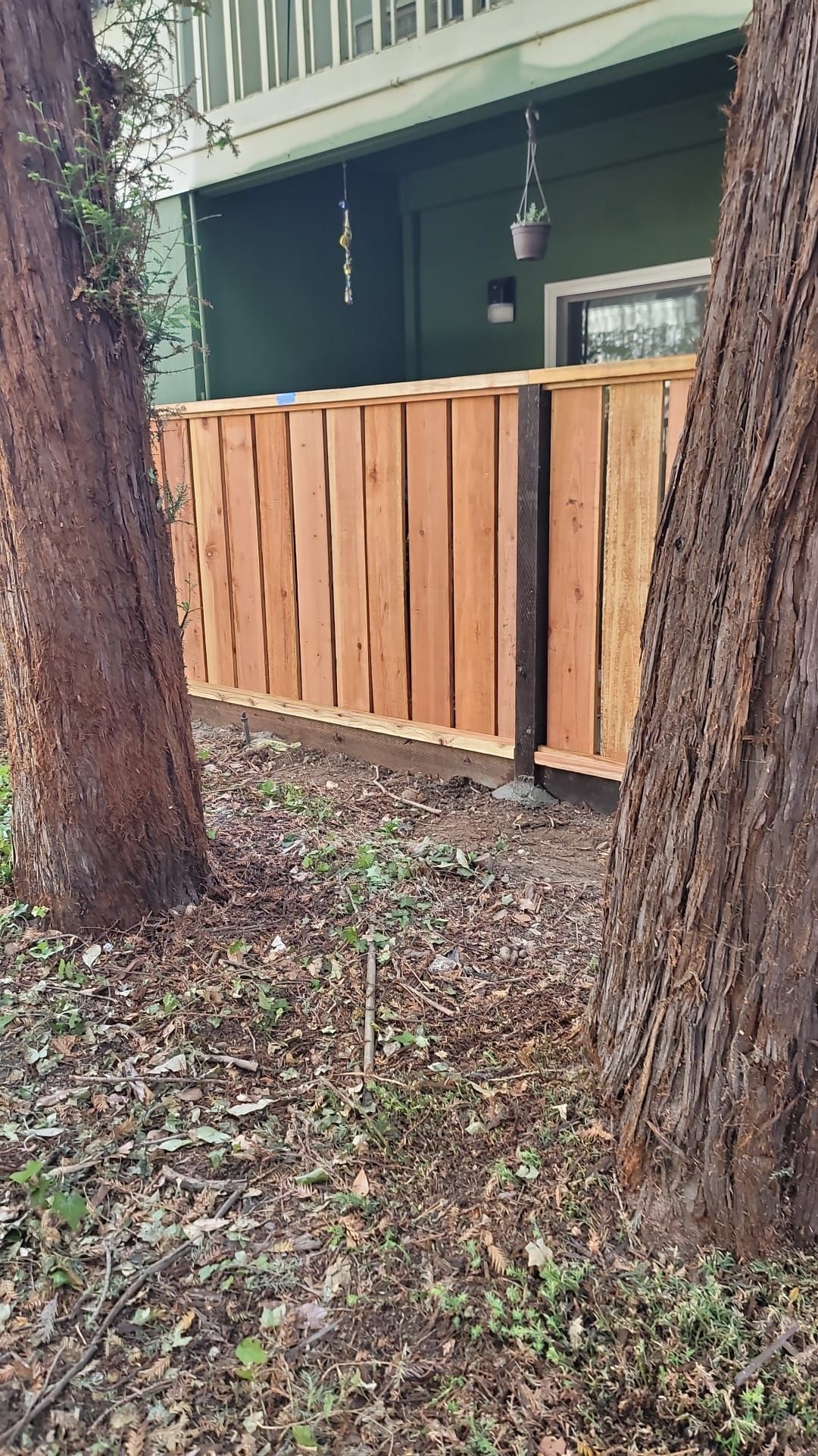 Wooden fence between two trees in front of a green building with porch.