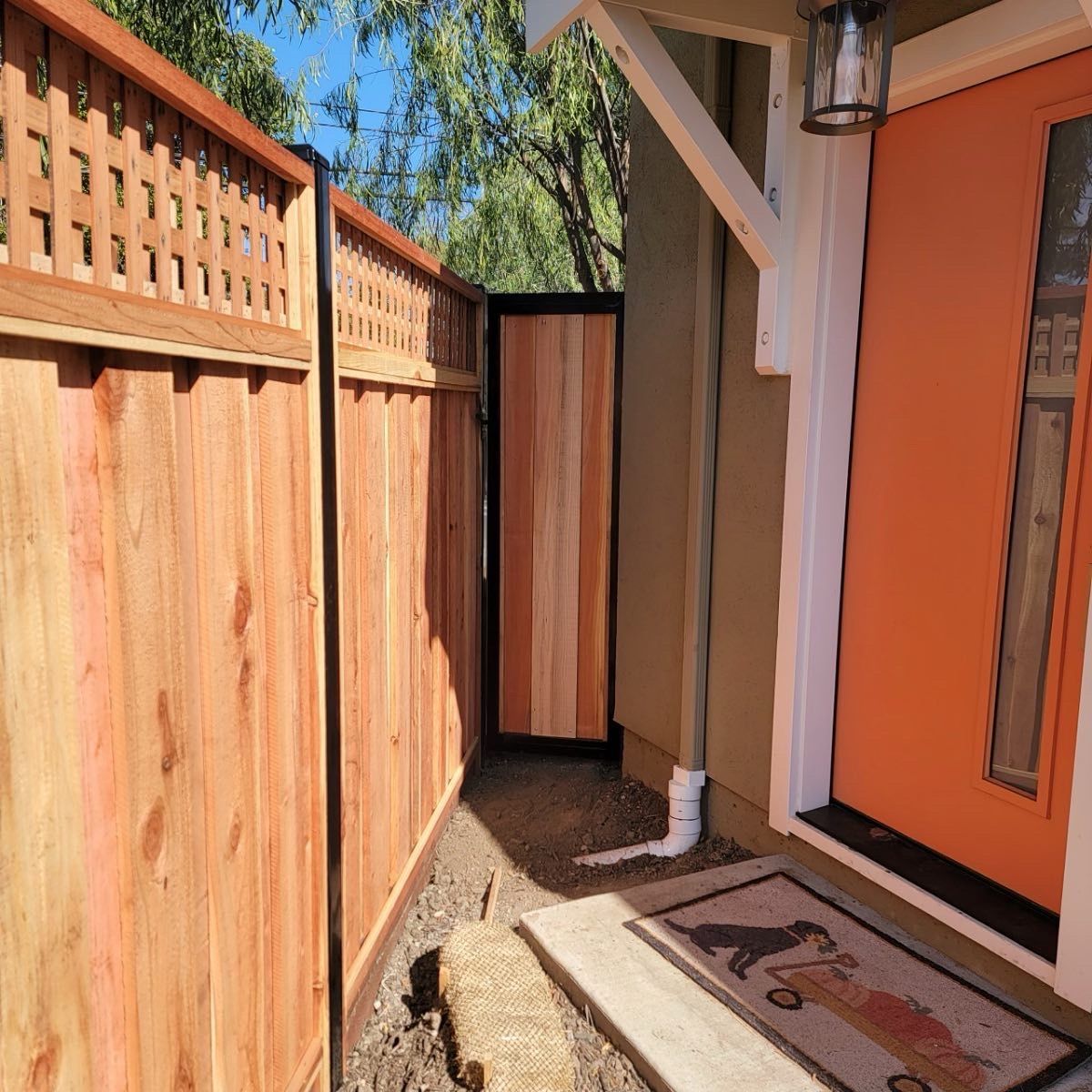 Wooden fence and gate leading to an orange front door. A welcome mat is at the entrance.