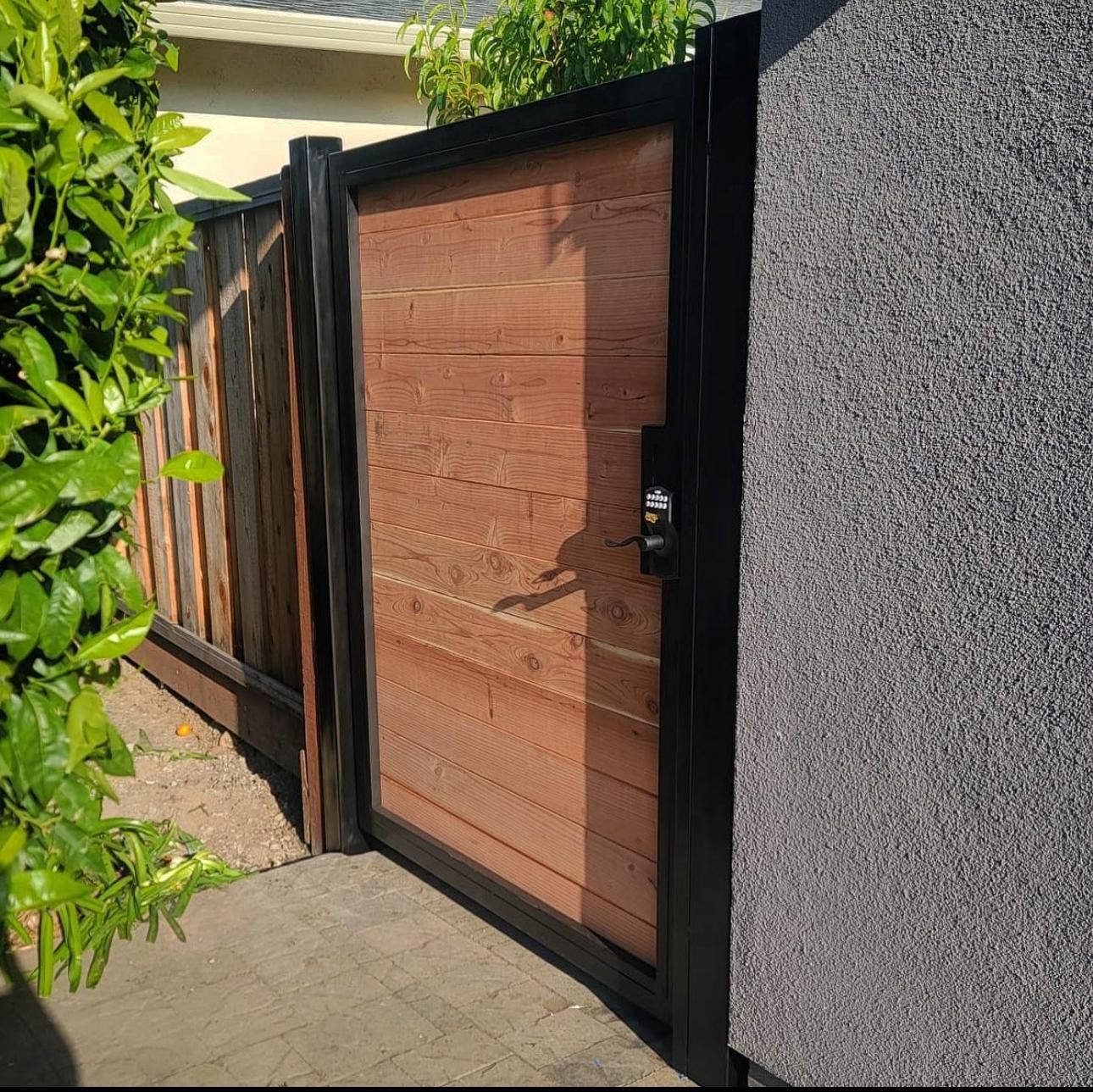 Wooden gate with black frame, next to fence and textured wall.