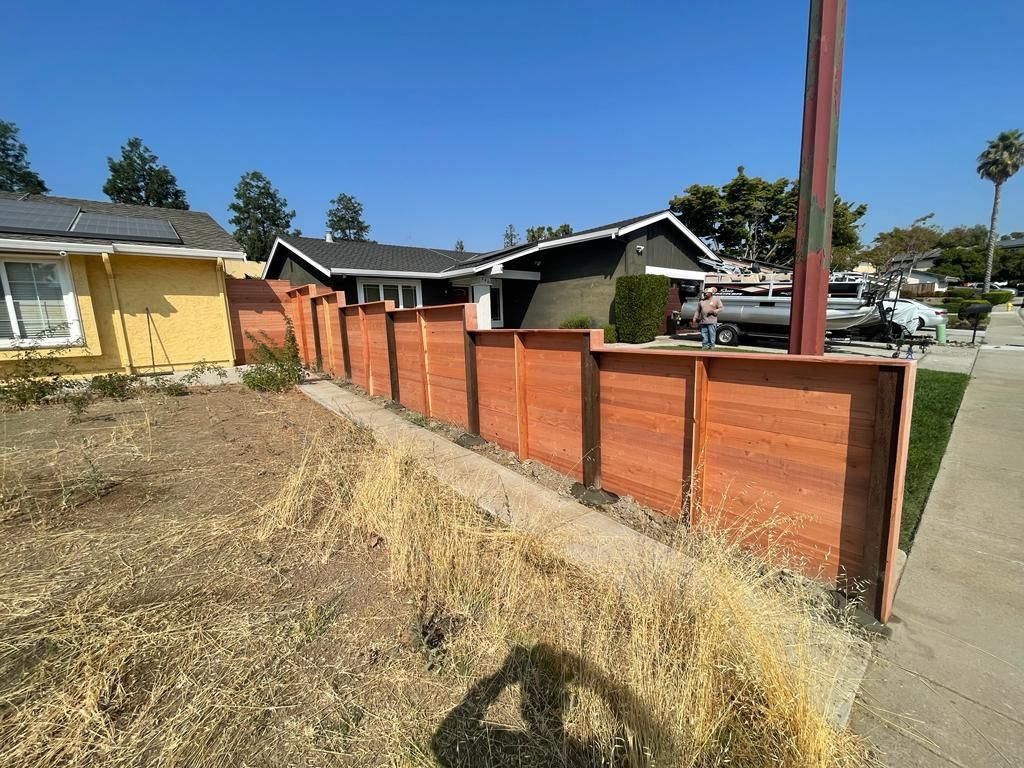 A new wooden fence surrounds a house and yard with dry grass under a clear blue sky.
