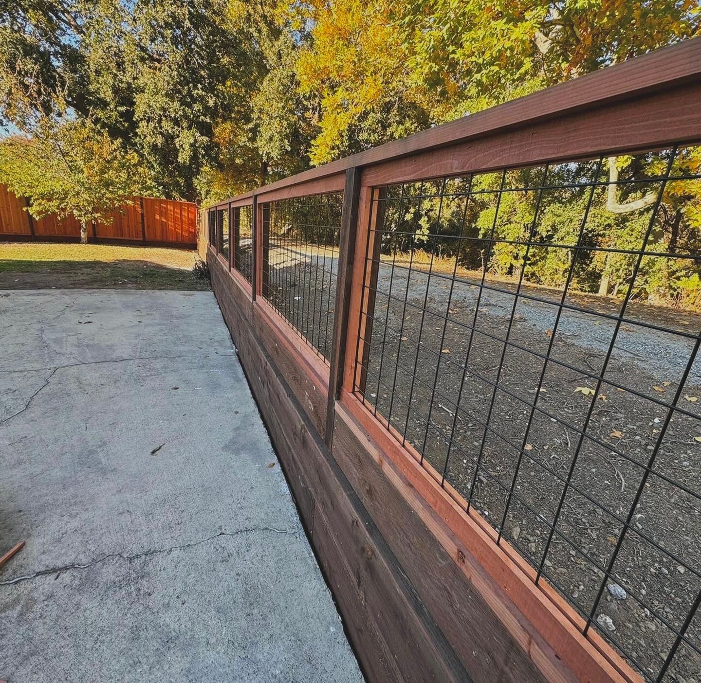 Wooden and wire fence in a yard with trees and a concrete ground.