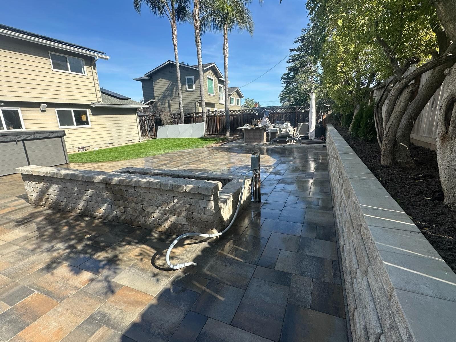 Backyard with stone patio, retaining wall, and two-story houses in background.