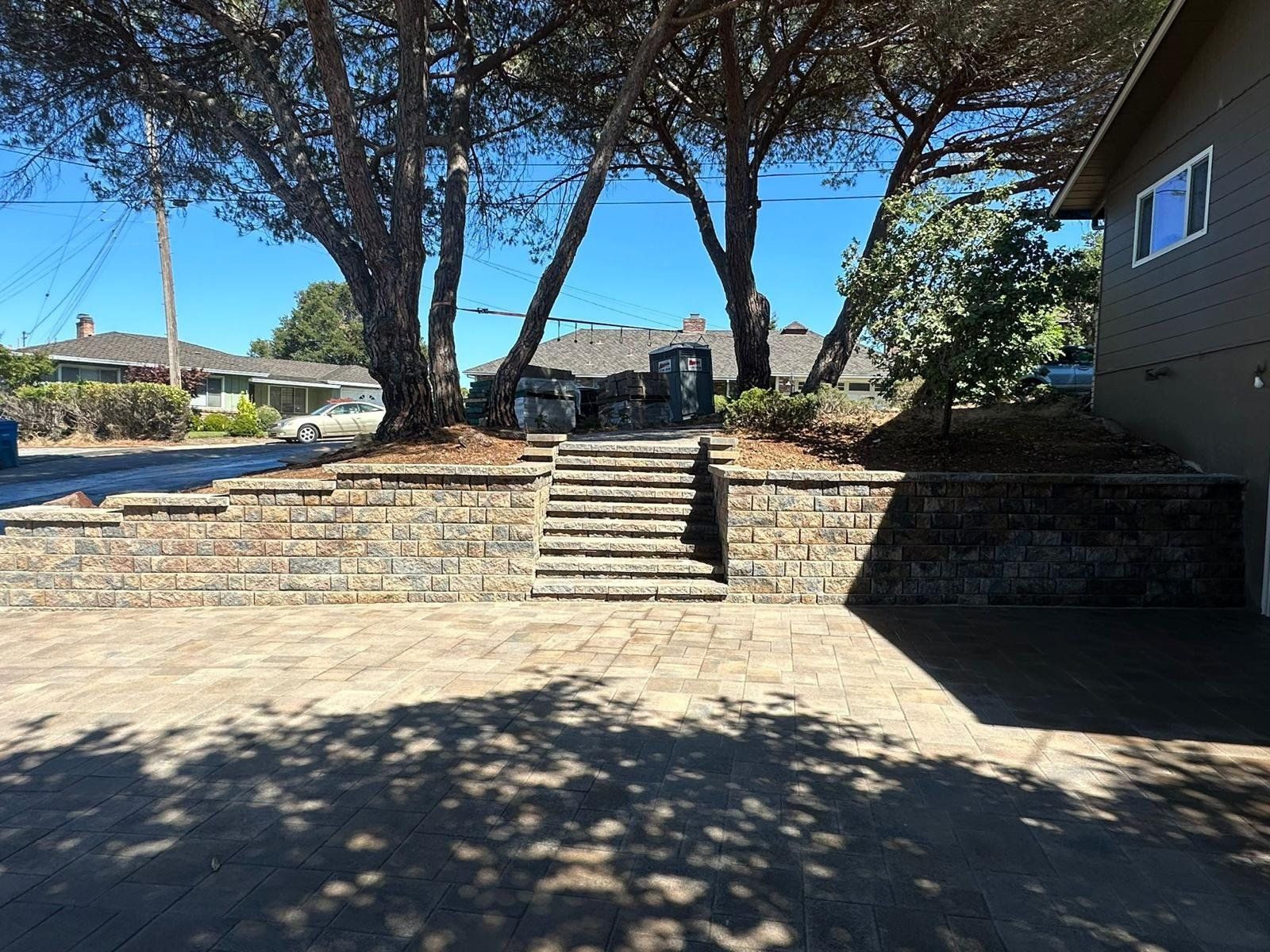 Stone steps and retaining walls leading to a grassy area with trees, next to a house.