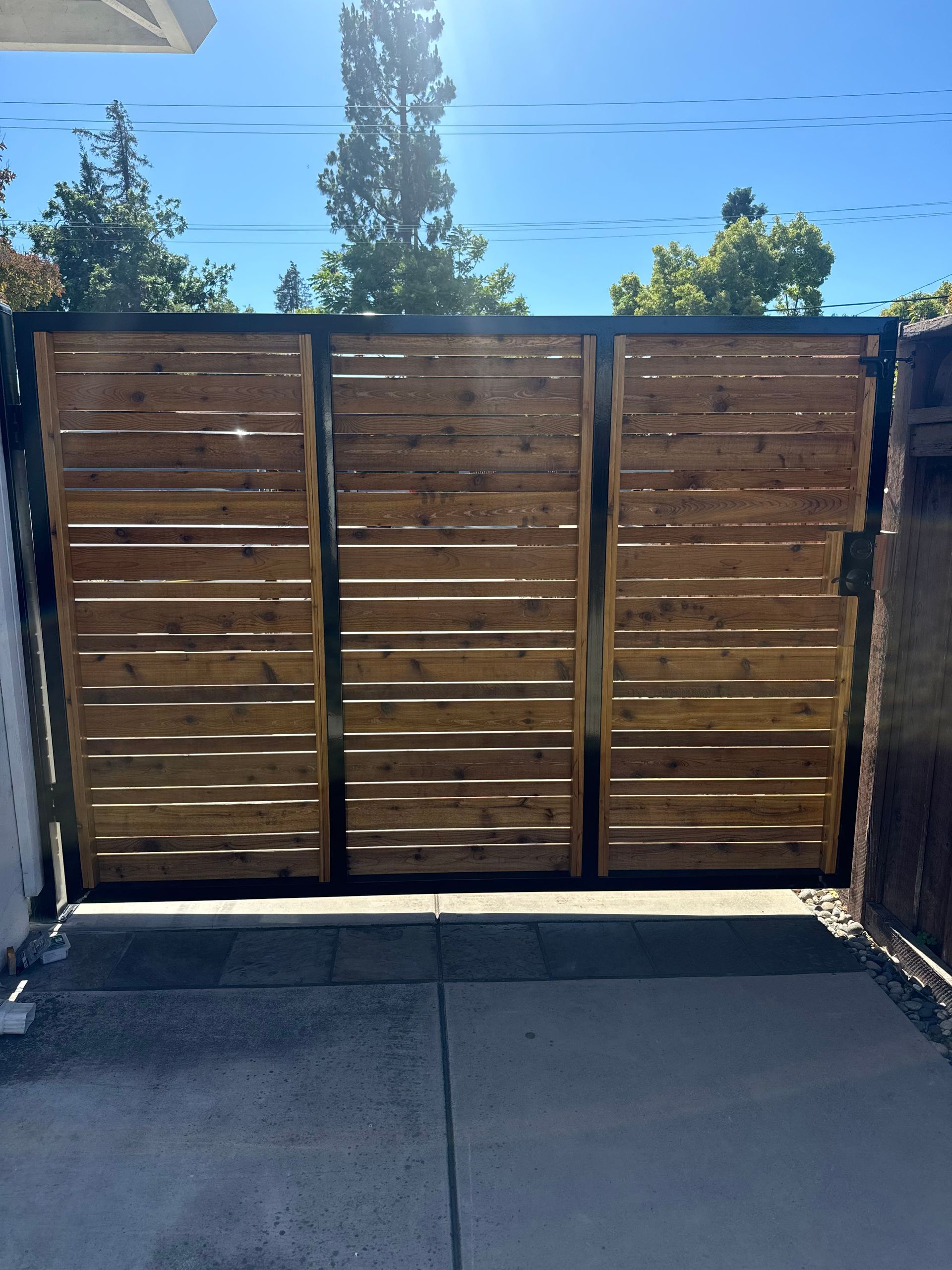 A modern driveway gate made of horizontal wooden planks inside a black metal frame.
