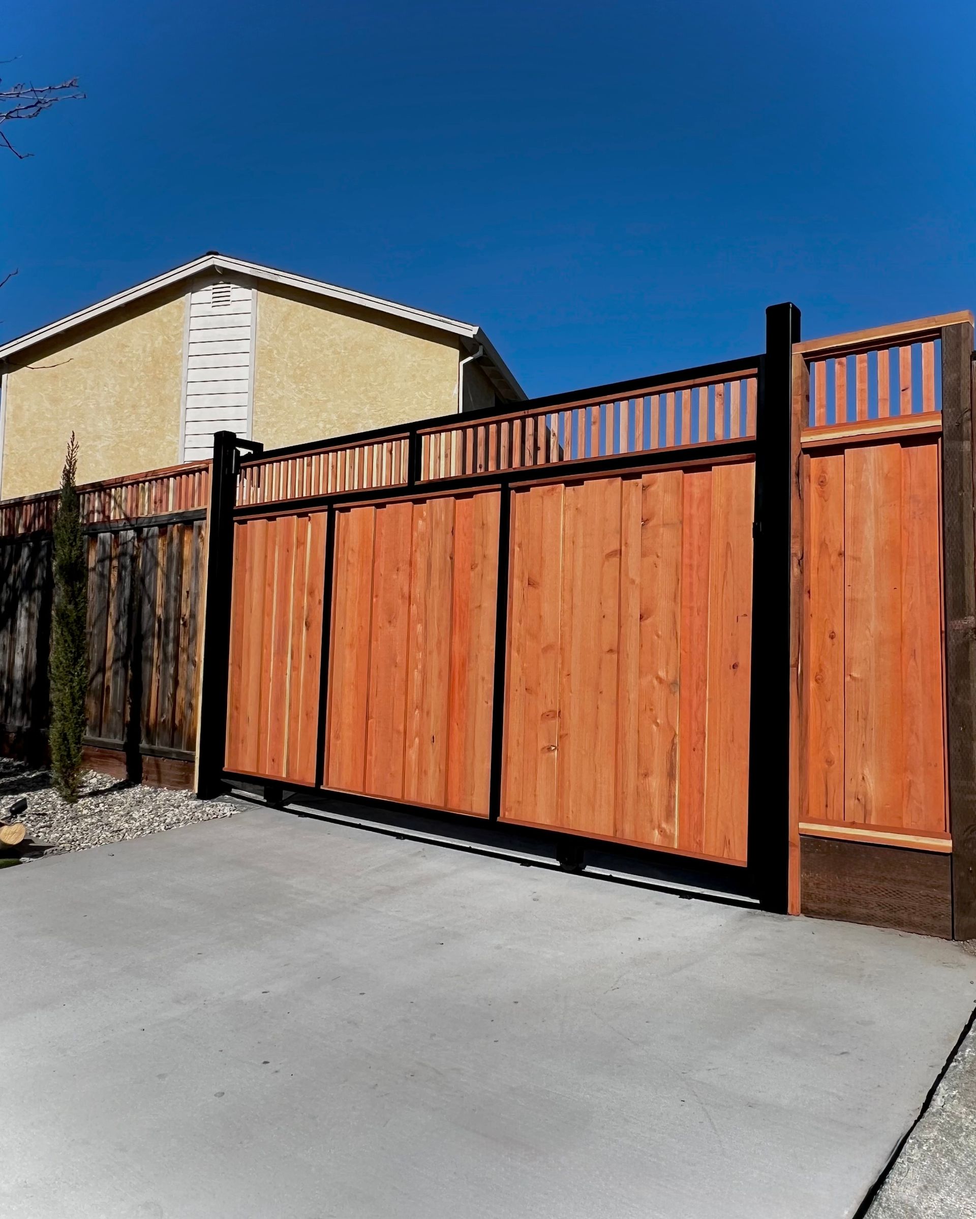 Orange wooden fence and gate beside a driveway under a clear blue sky.