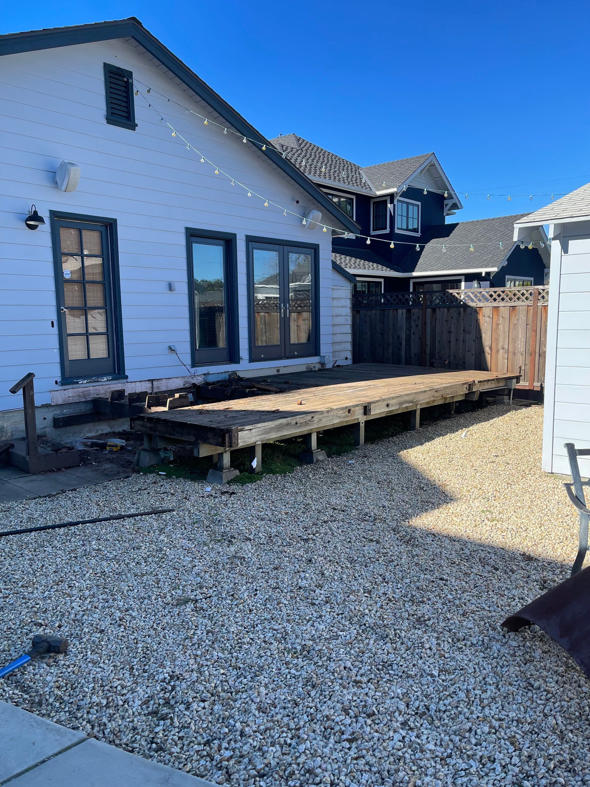 A white house with a partially demolished wooden deck in a yard covered with light-colored gravel.