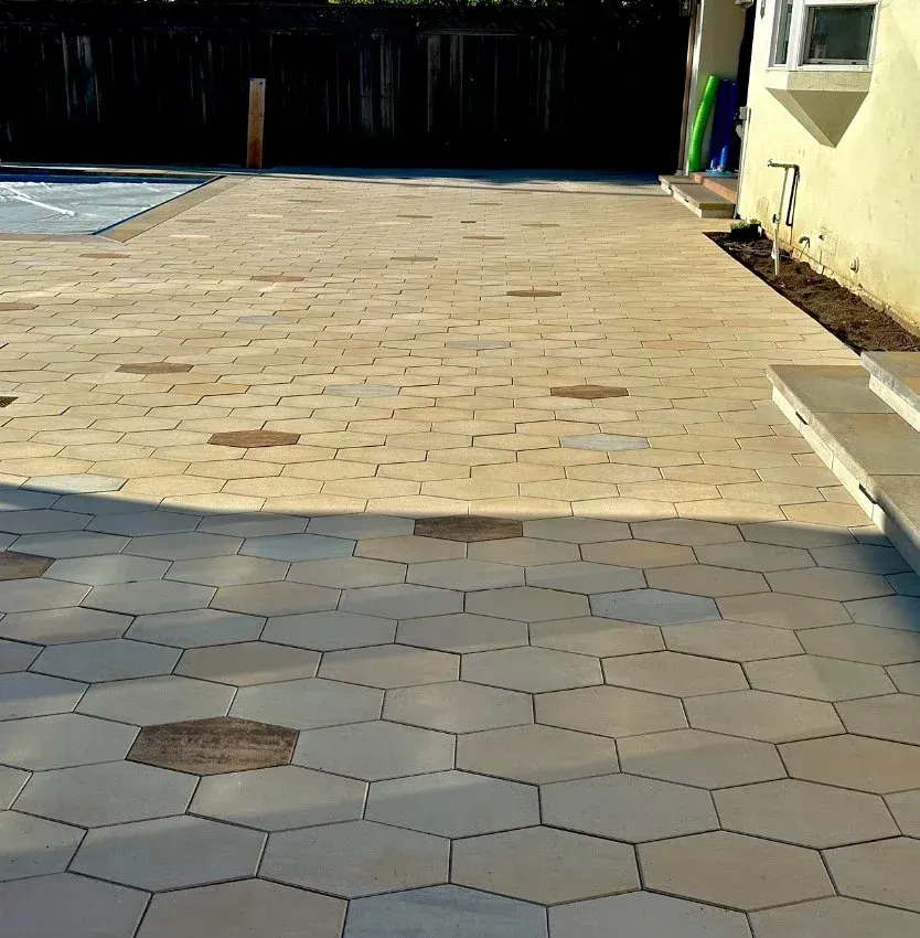 Hexagonal pavers on a patio with a dark fence and part of a building in the background.