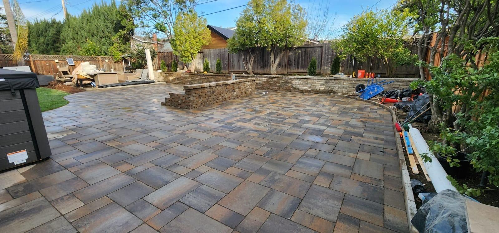 A newly installed stone paver patio in a backyard with a low retaining wall and surrounding garden area.