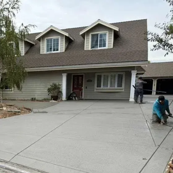 New concrete driveway being installed in front of a house. Two workers are on the driveway, one is kneeling.