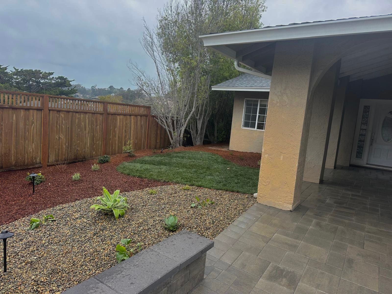 Front yard with stone path, gravel beds, mulch, green grass, and wooden fence.