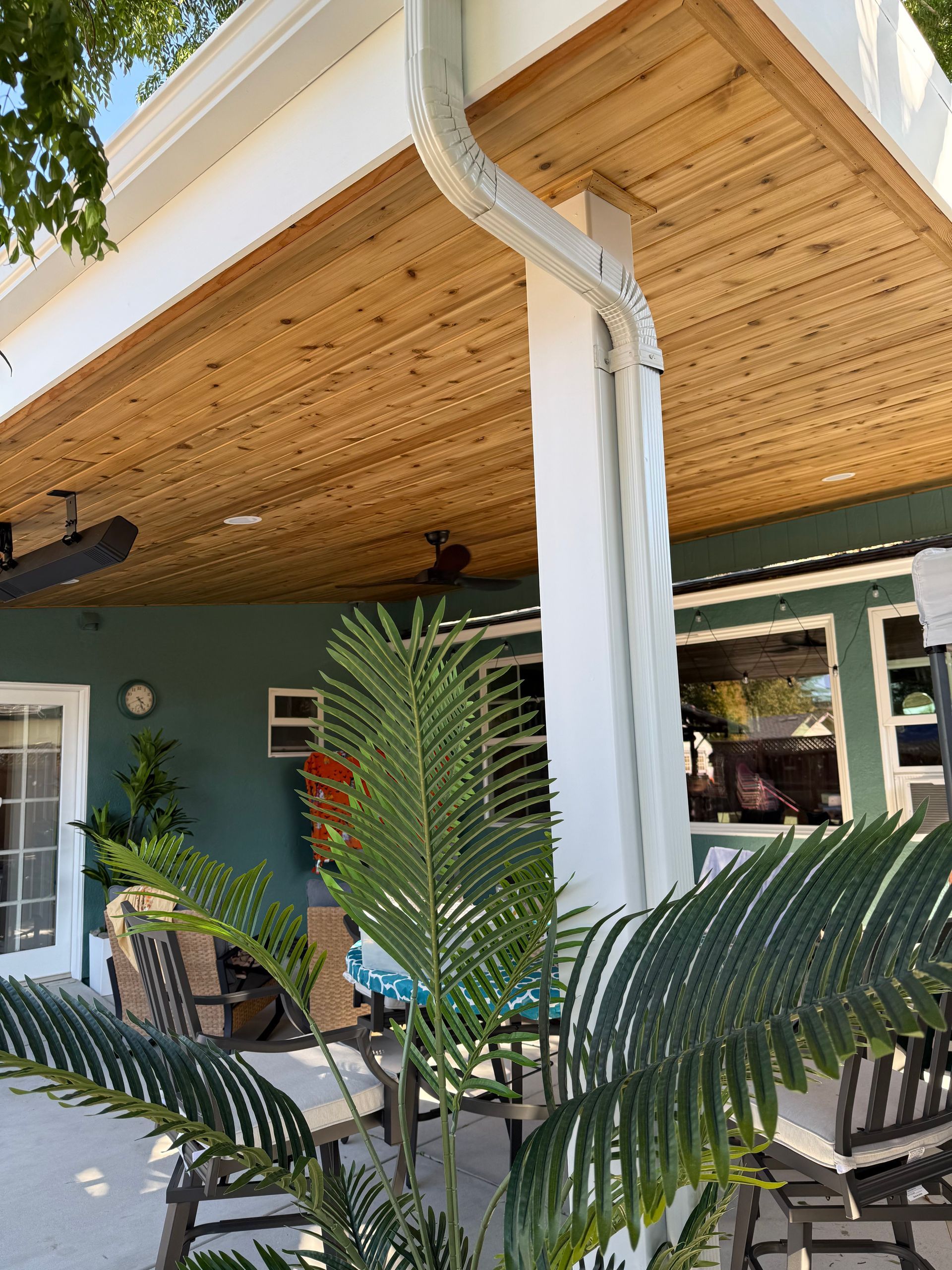 Patio with wood ceiling, white column, and green wall. Palm fronds in foreground.