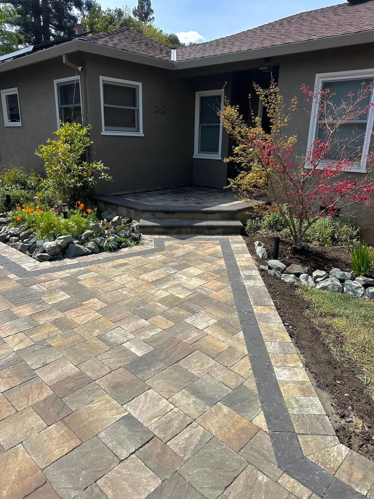 Brick paved walkway leading to a house with garden beds on either side.