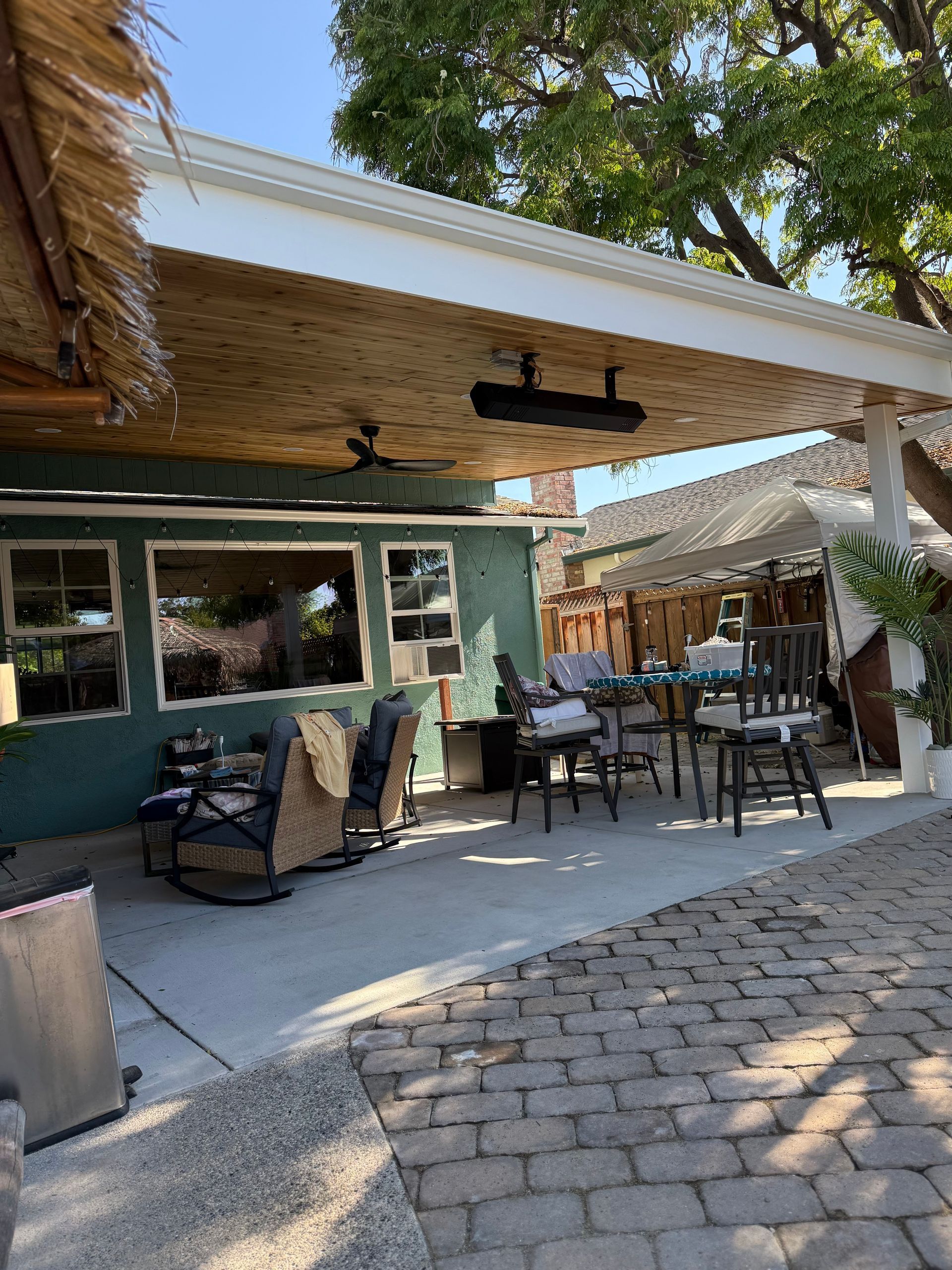 Backyard patio with seating, overhead cover, and a dining area, on a sunny day.