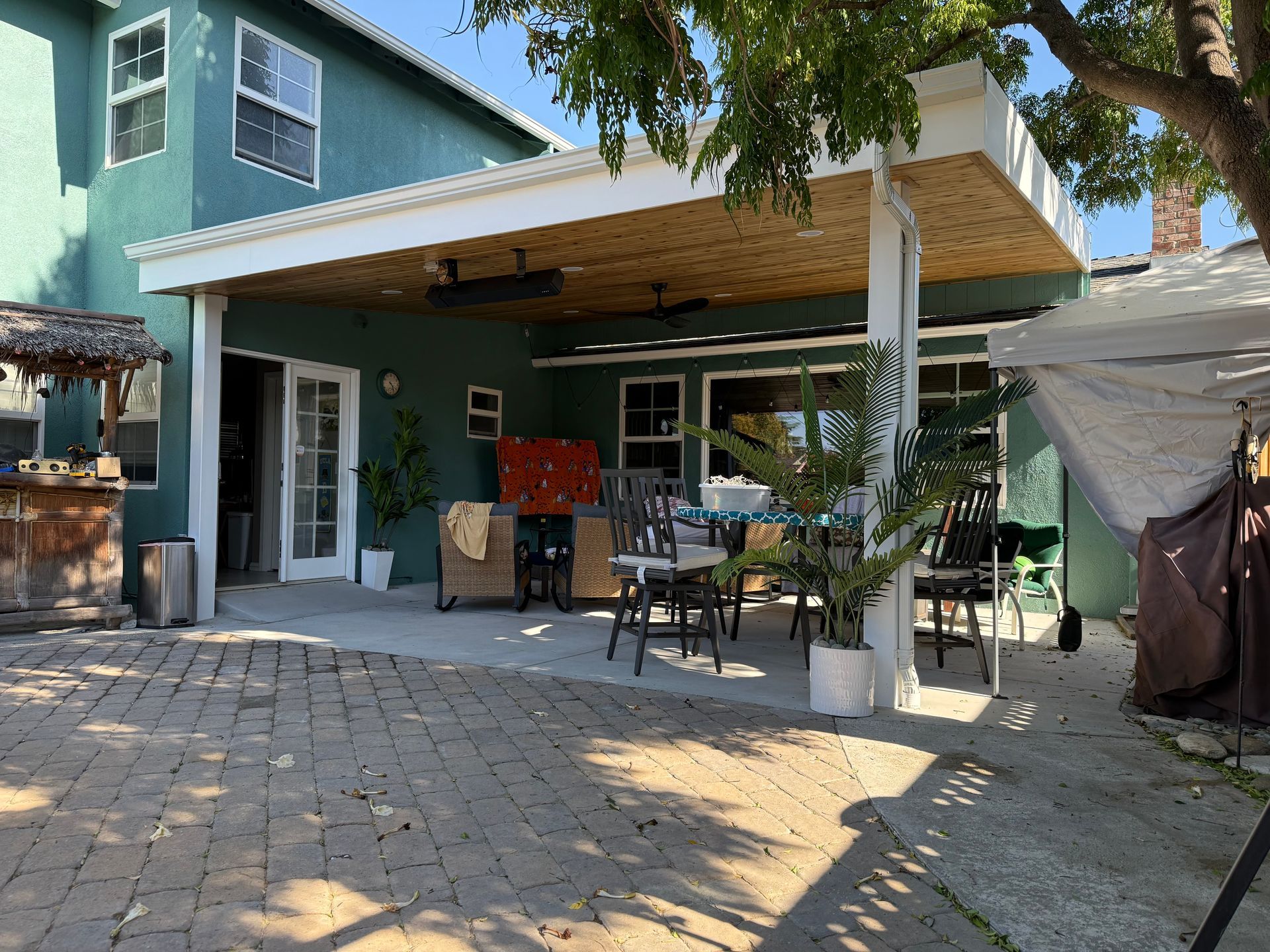Backyard patio with green house, covered seating area, and brick pavers.