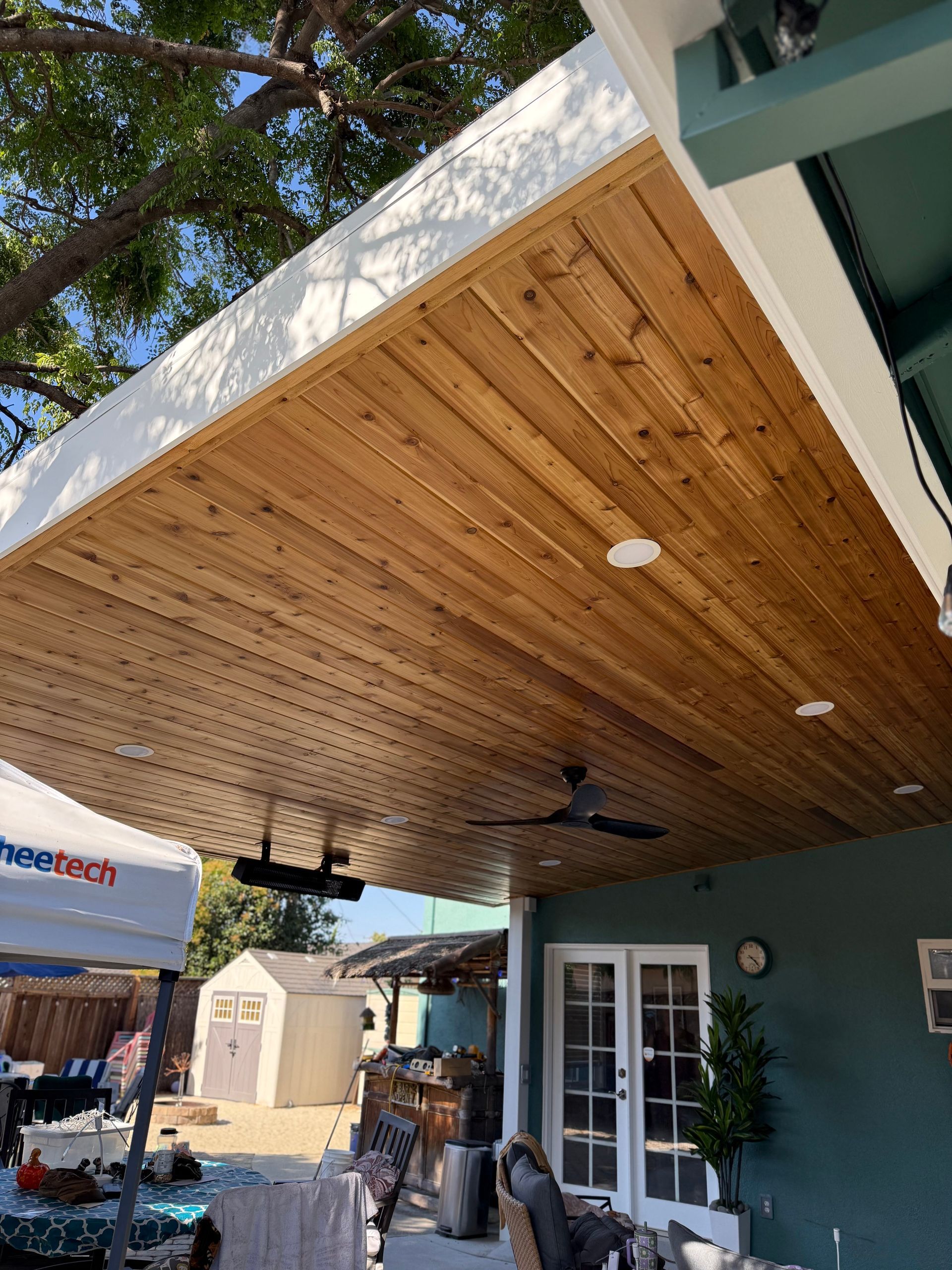 Wooden patio ceiling with recessed lights and ceiling fans. Turquoise building exterior with double doors.