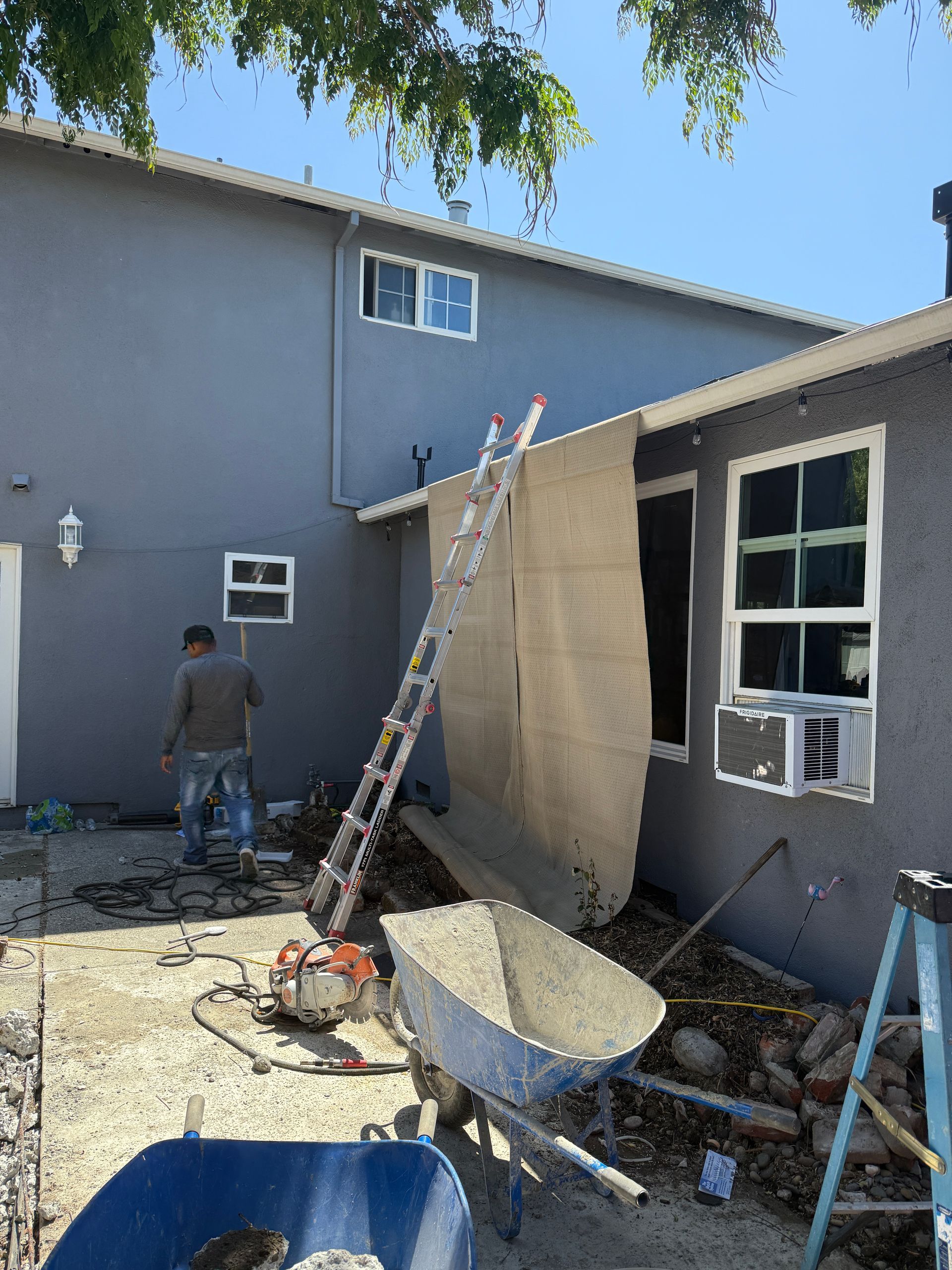 Construction scene with a worker, ladder, and building. Gray exterior, blue sky, and construction tools.