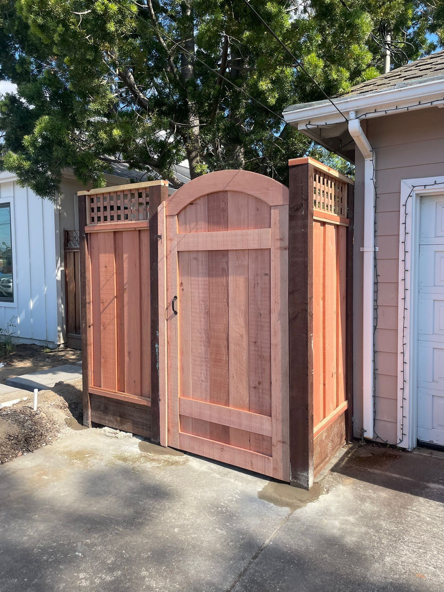 A new arched wooden gate flanked by matching wooden fence panels with lattice tops, installed next to a house.