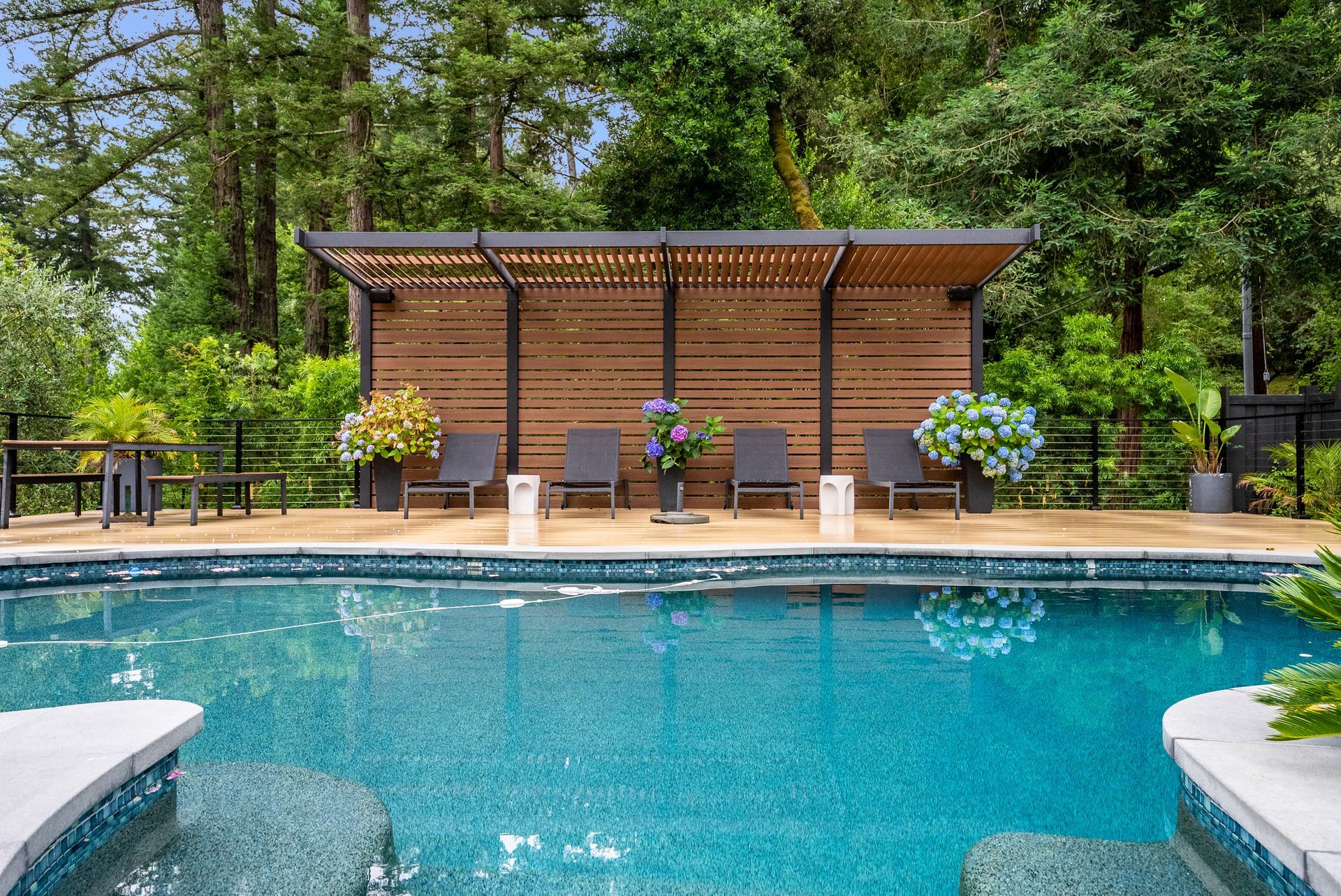 Backyard pool with a wooden cabana, lounge chairs, and lush trees surrounding the deck.