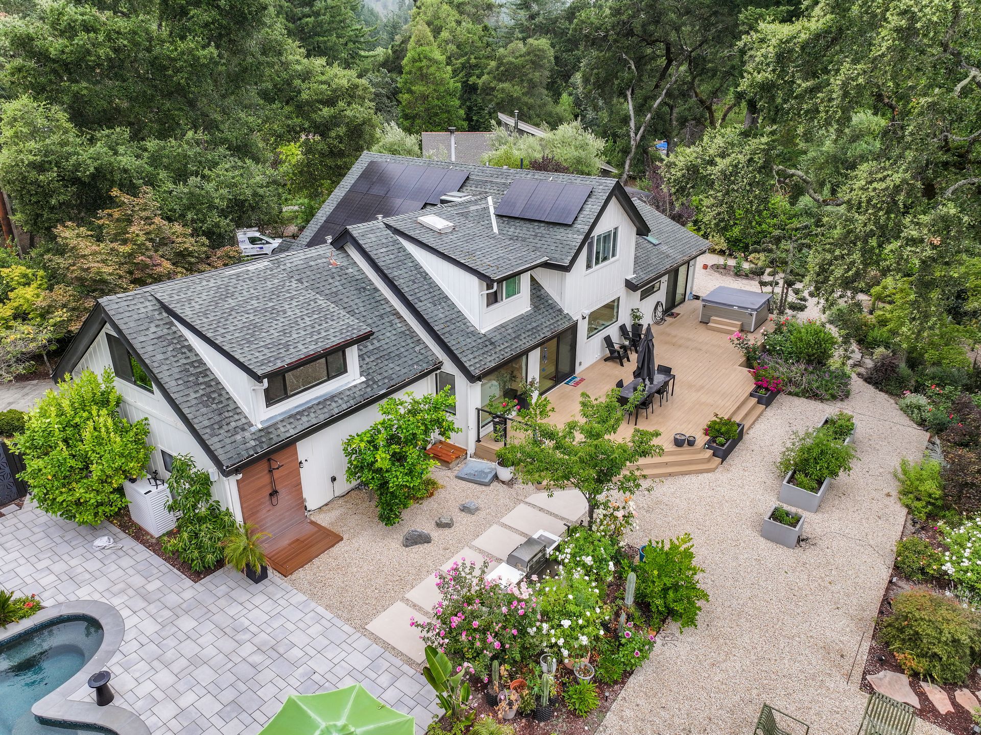 Aerial view of a white countryside house with a slate roof, patio, and garden surrounded by trees