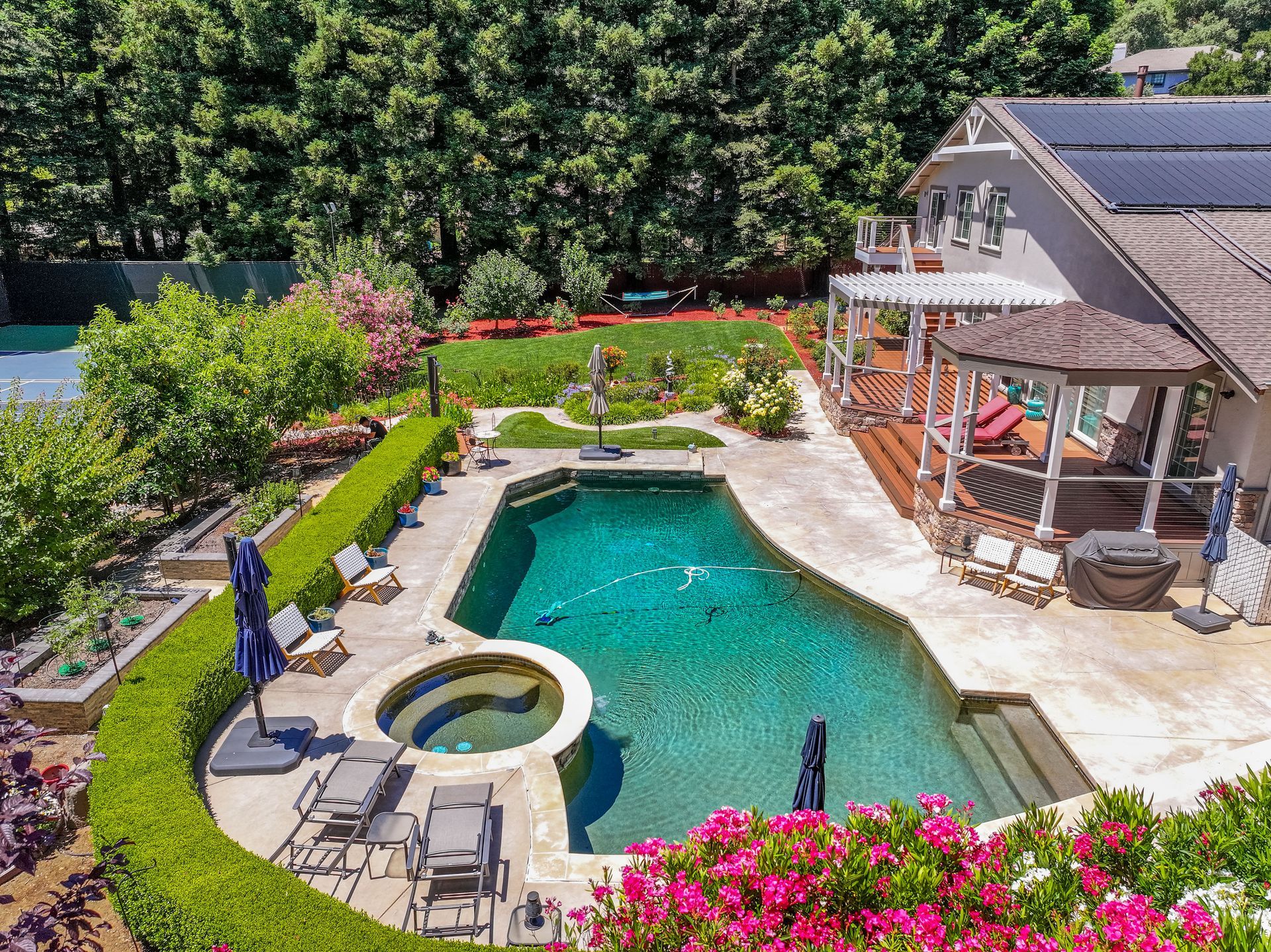 Backyard pool and hot tub beside a patio, with lounge chairs and lush greenery.