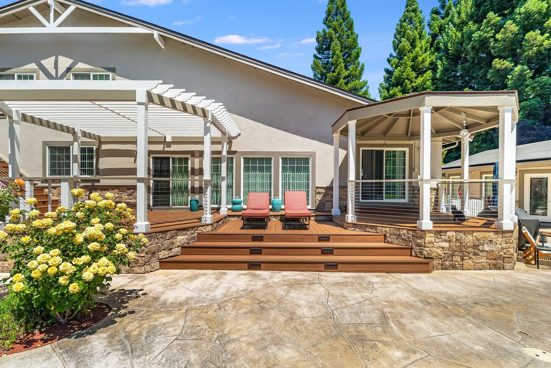 Backyard patio with wooden deck, pergola, outdoor seating, and a house exterior on a sunny day