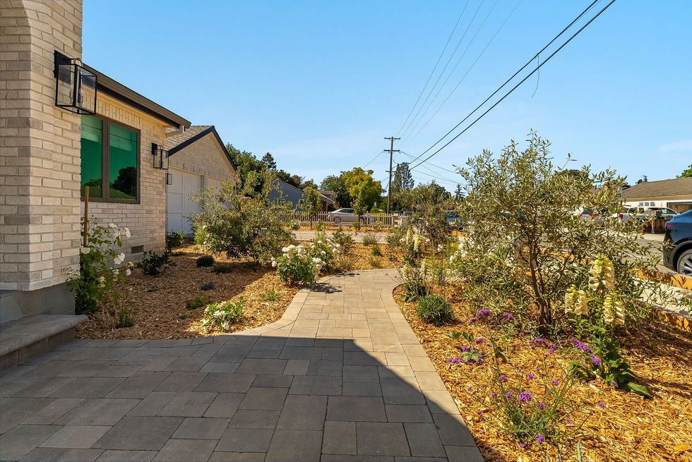 Stone house beside a paved walkway through a sunny desert garden with shrubs and purple flowers