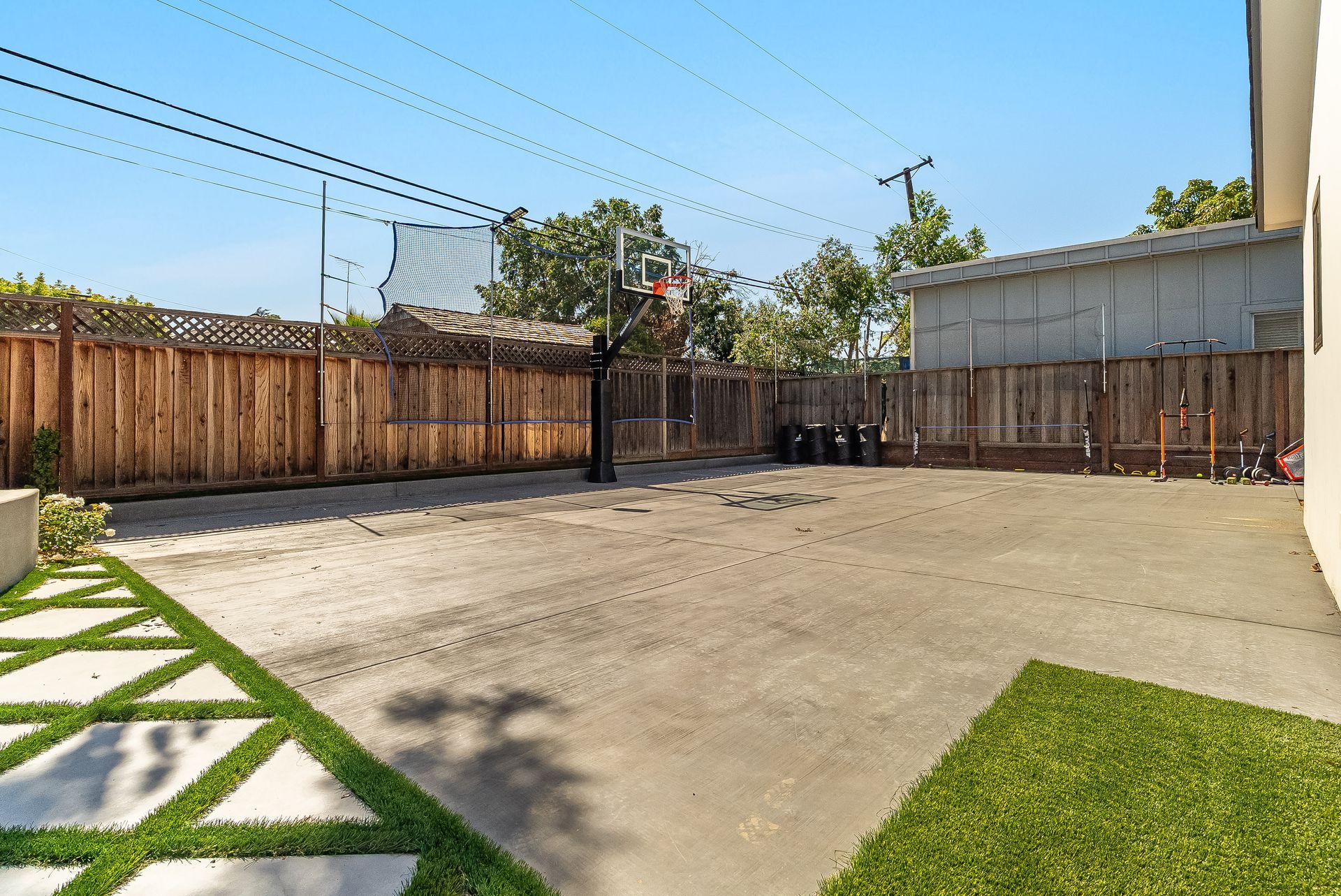 Backyard patio with concrete ground, wooden fence, and green lawn under a clear blue sky