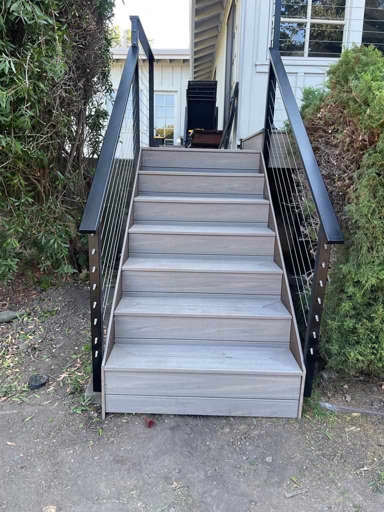 Wooden staircase with black metal railings, leading up to a white building.